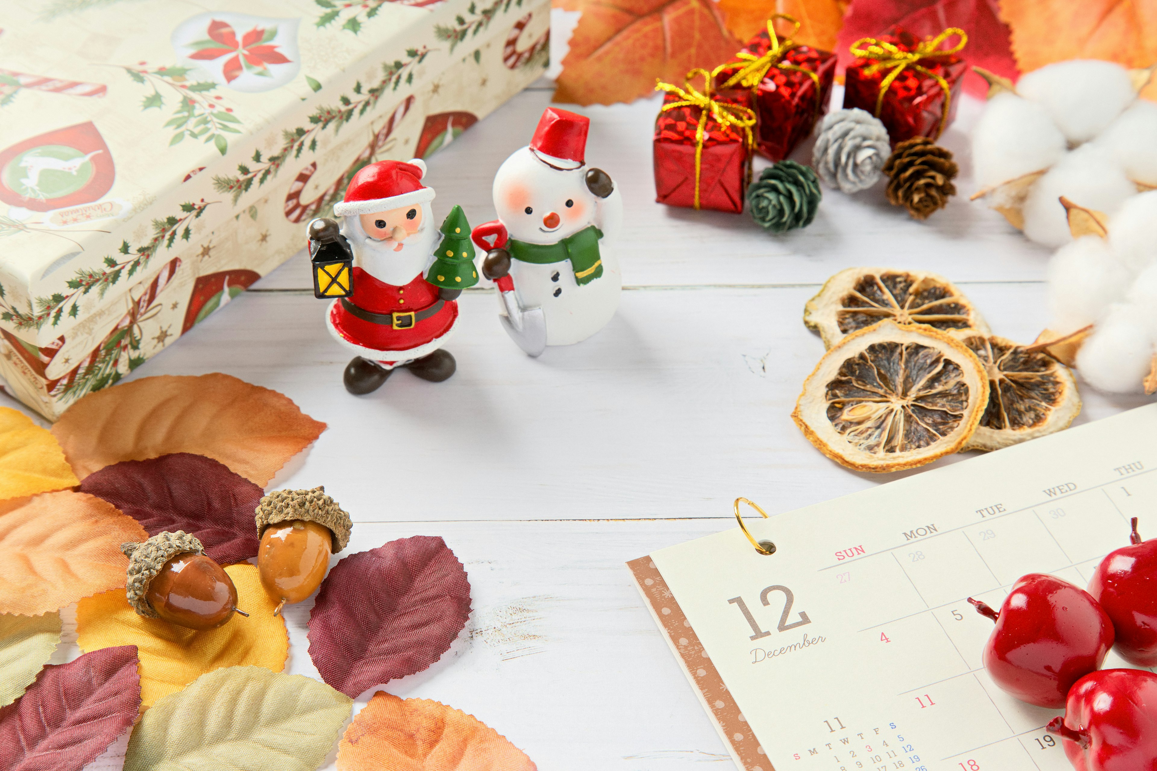 Composizione su tavolo con statuette di Babbo Natale e pupazzo di neve circondate da regali di Natale e foglie d'autunno