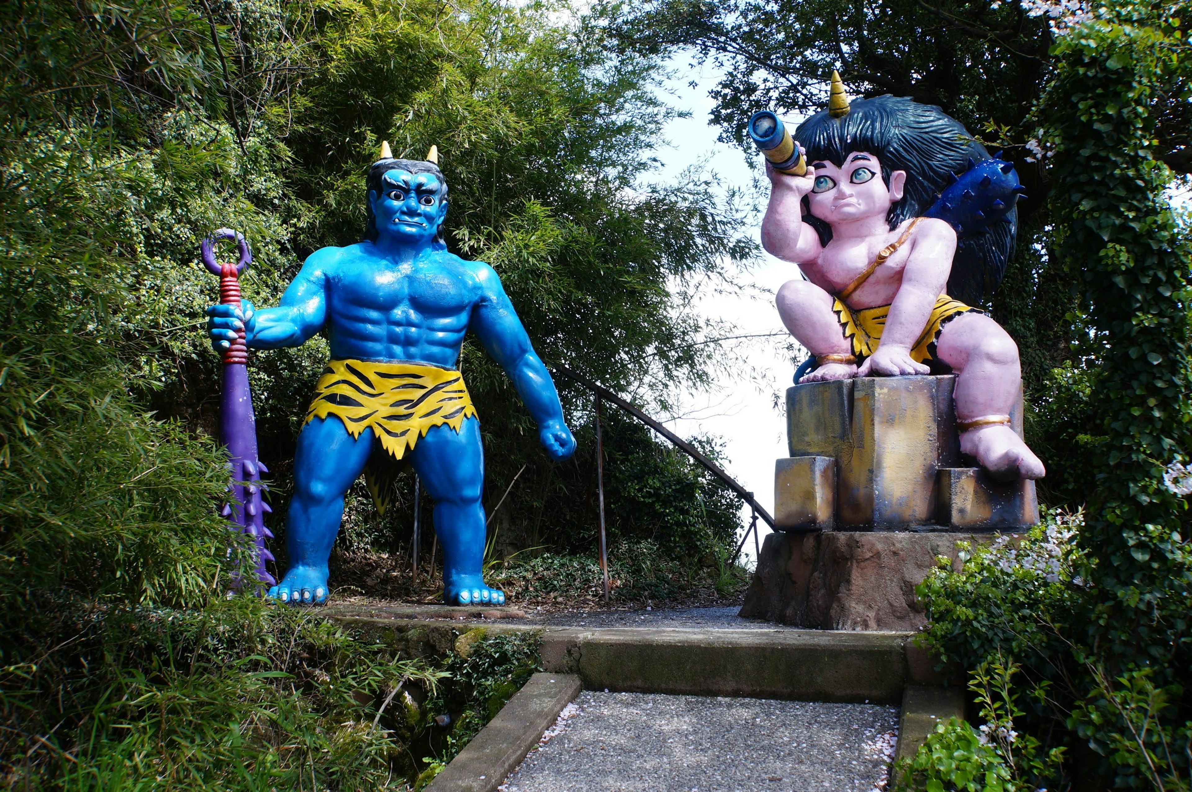 Image of a blue giant and a pink deity statue in a lush outdoor setting