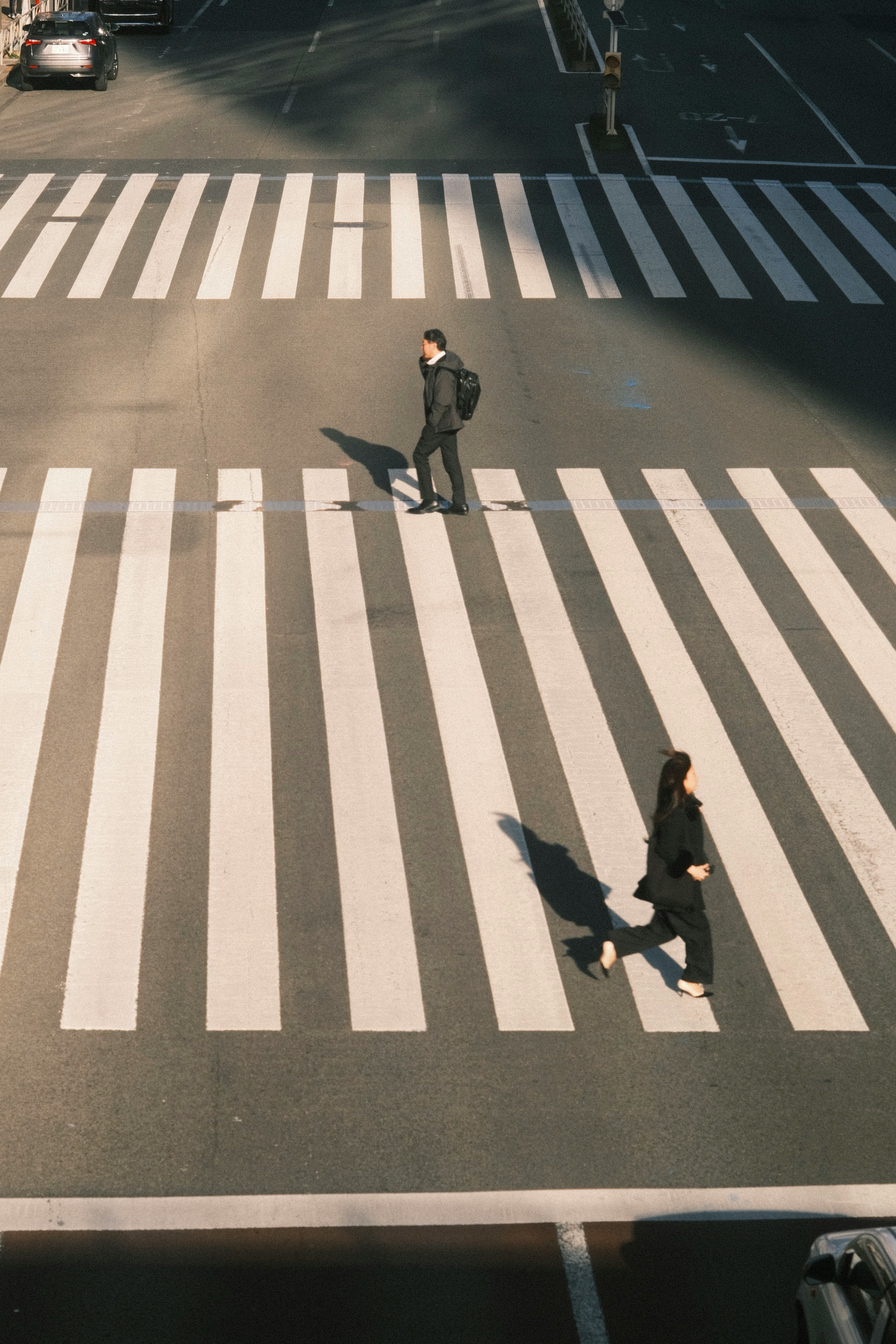 Two individuals walking across a white crosswalk with shadows