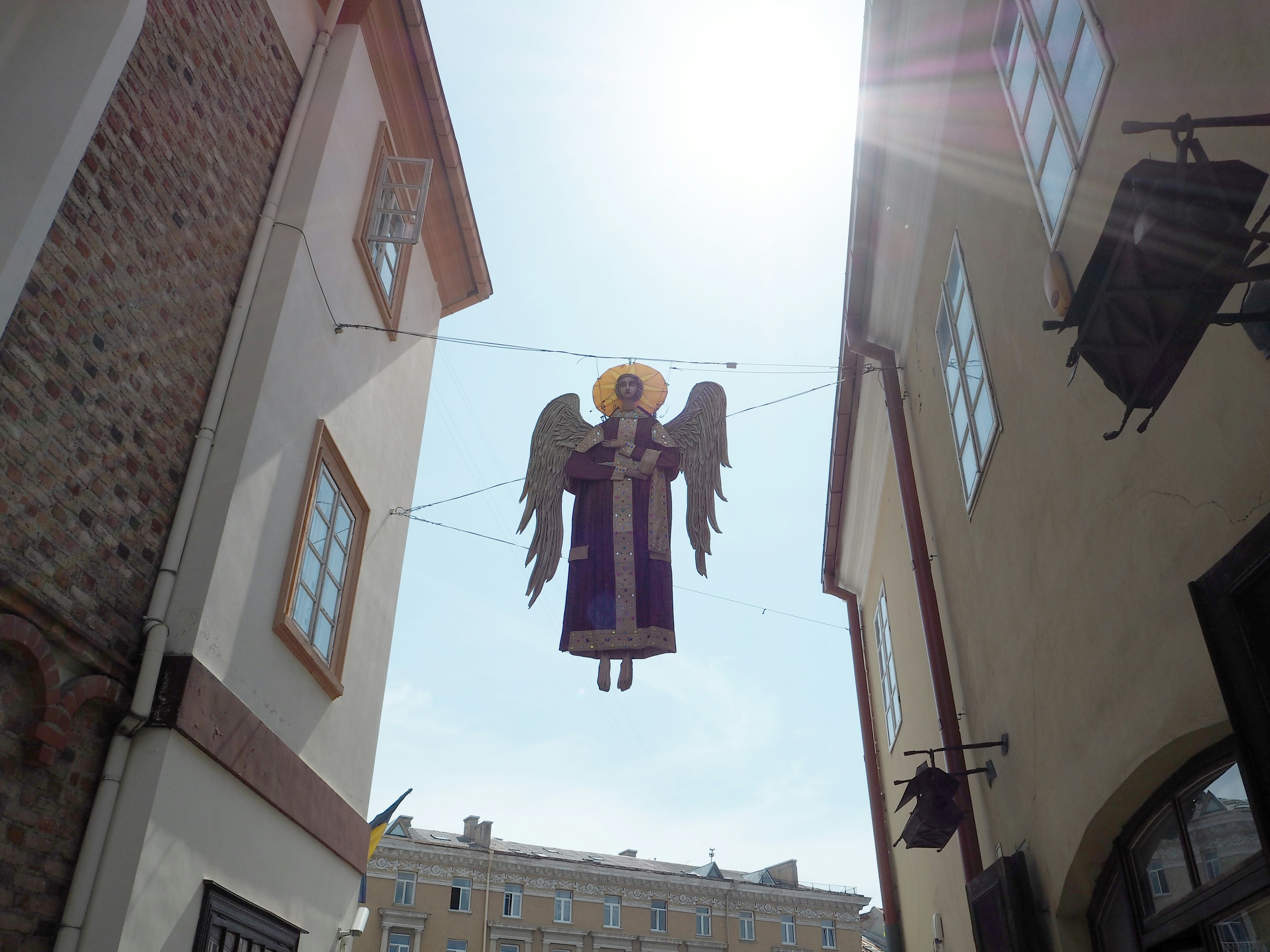 Una estatua de ángel con alas extendidas colgando en una calle estrecha bajo un cielo azul