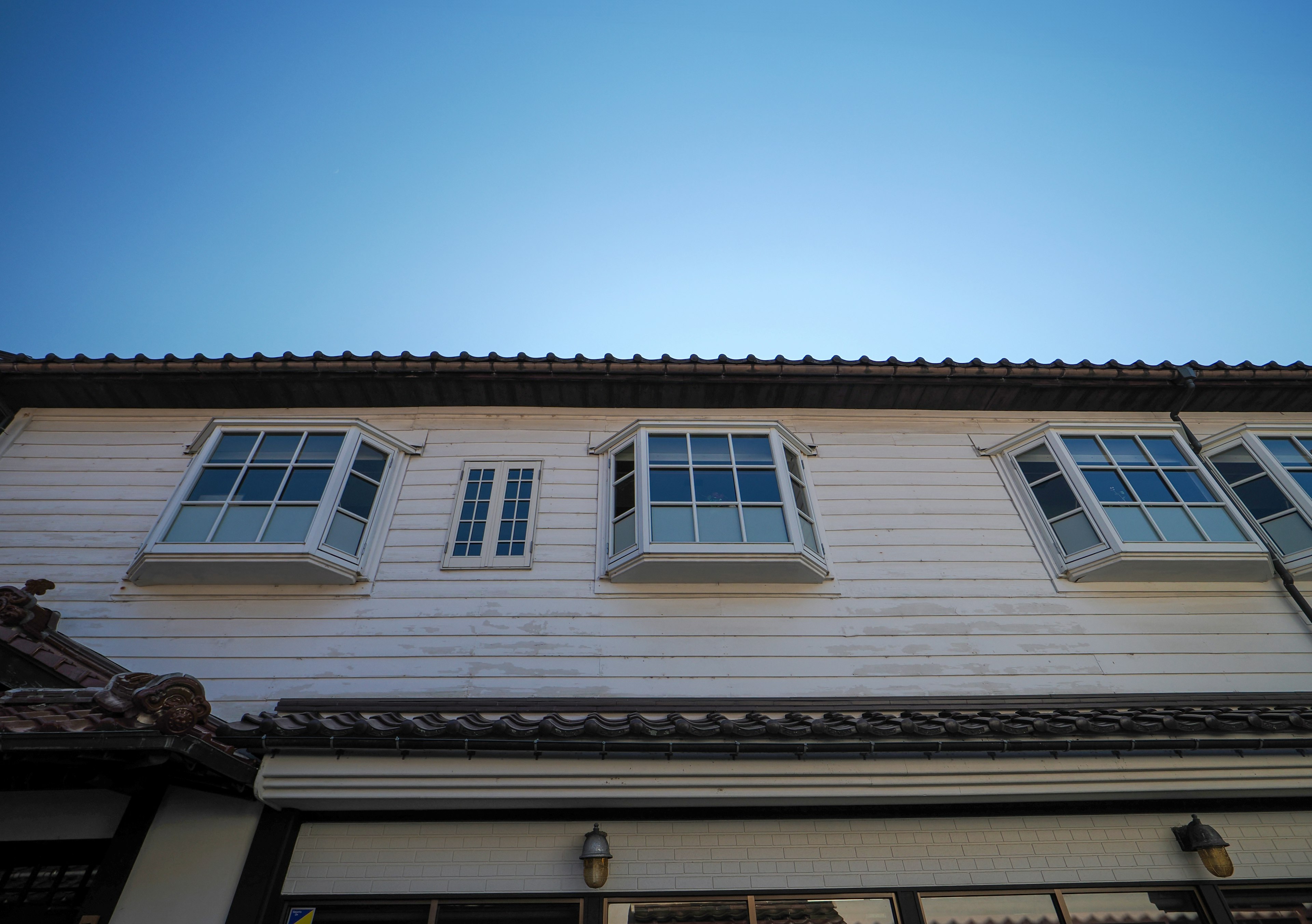 Casa de madera blanca con dos ventanas superiores bajo un cielo azul claro