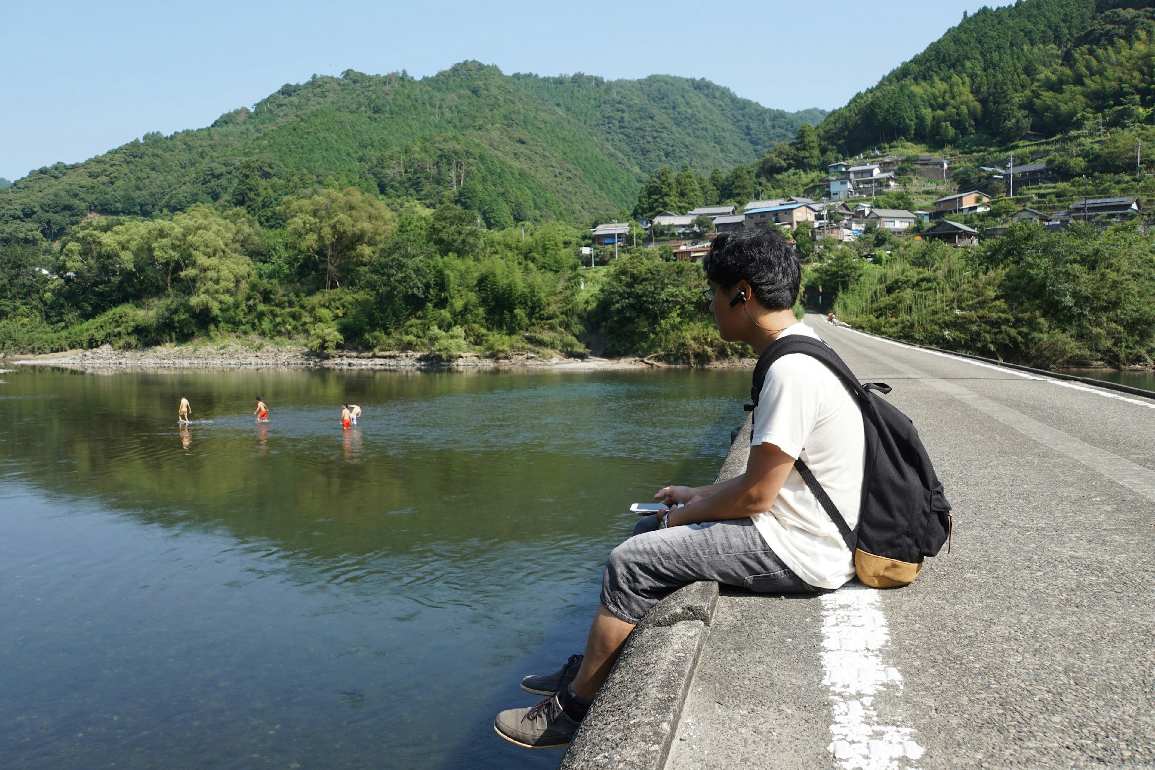 Hombre sentado junto al río con montañas de fondo