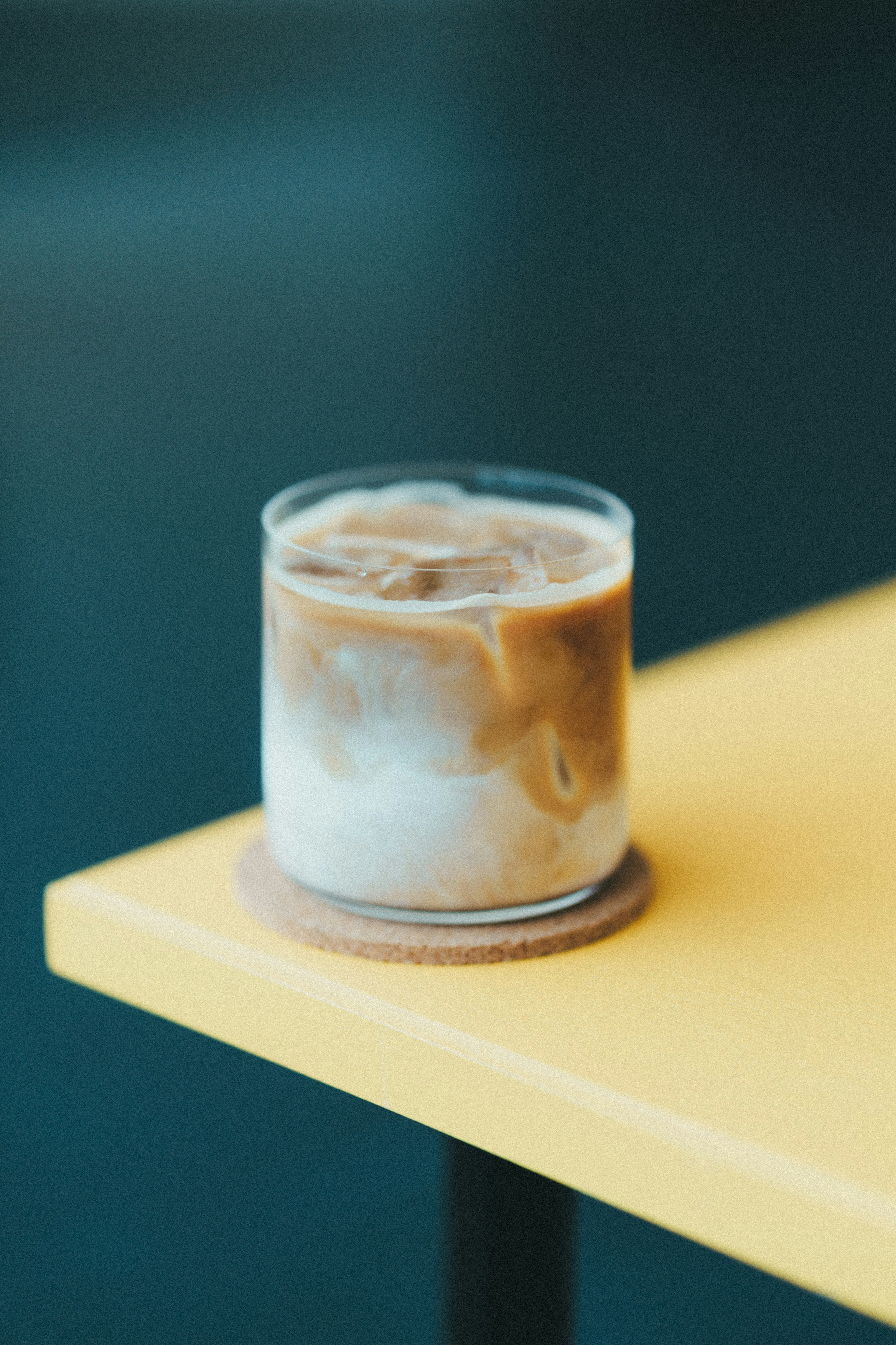 A glass of iced coffee on a yellow table with a cork coaster