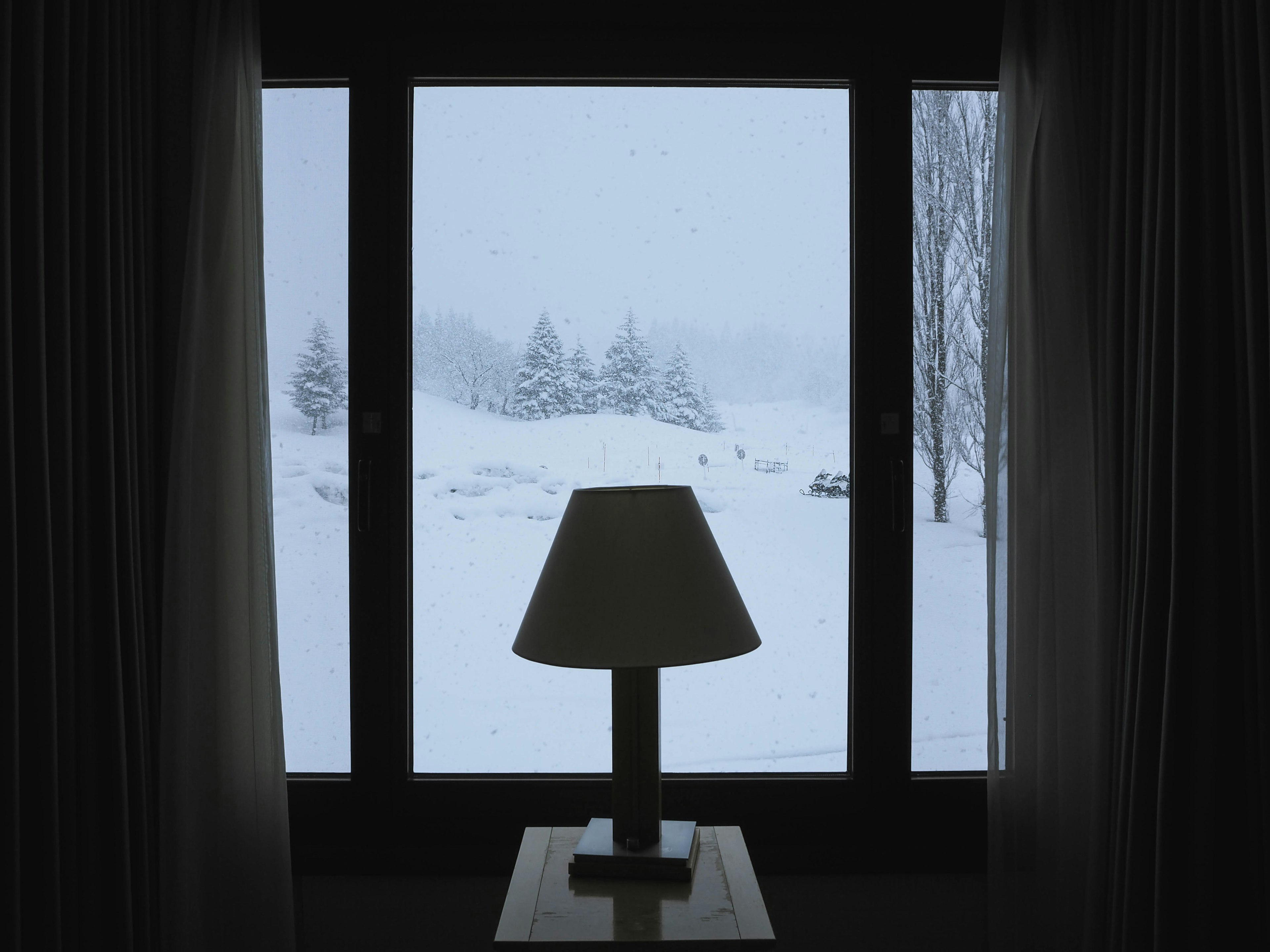 Silhouette of a table lamp with a snowy landscape visible through the window