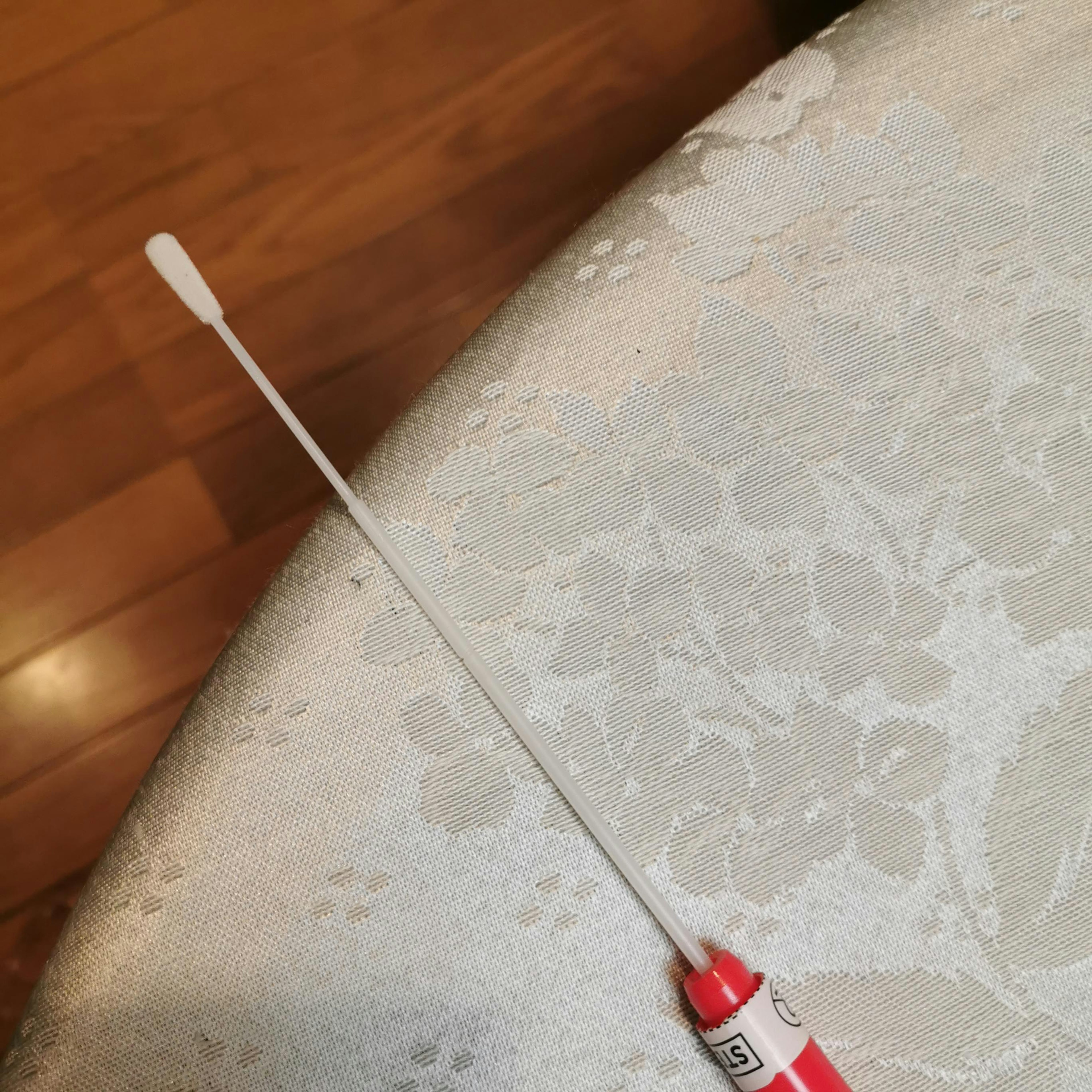 A long cotton swab with a red cap resting on a white tablecloth