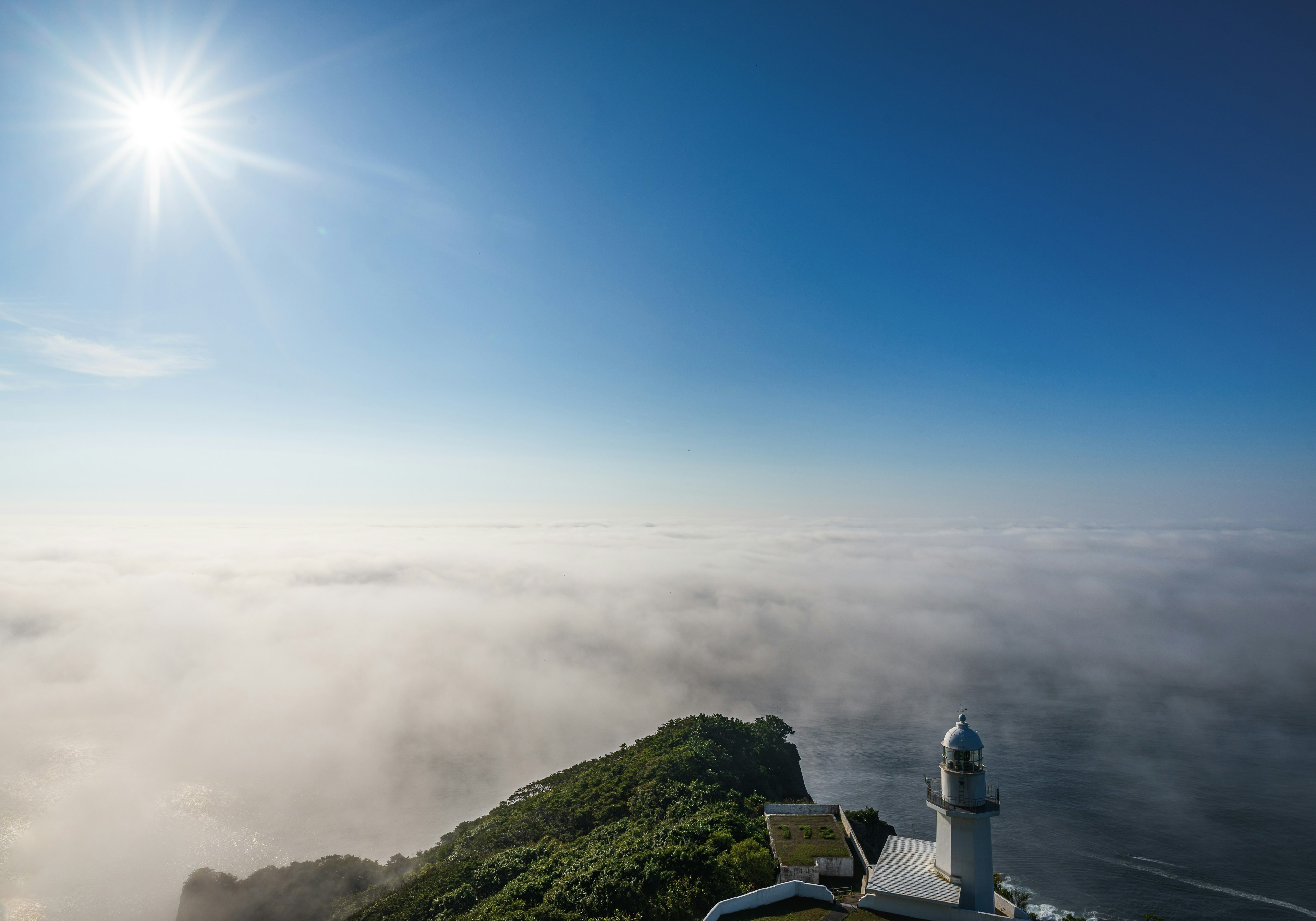 青空の下、霧に包まれた山の頂上にある灯台の景色