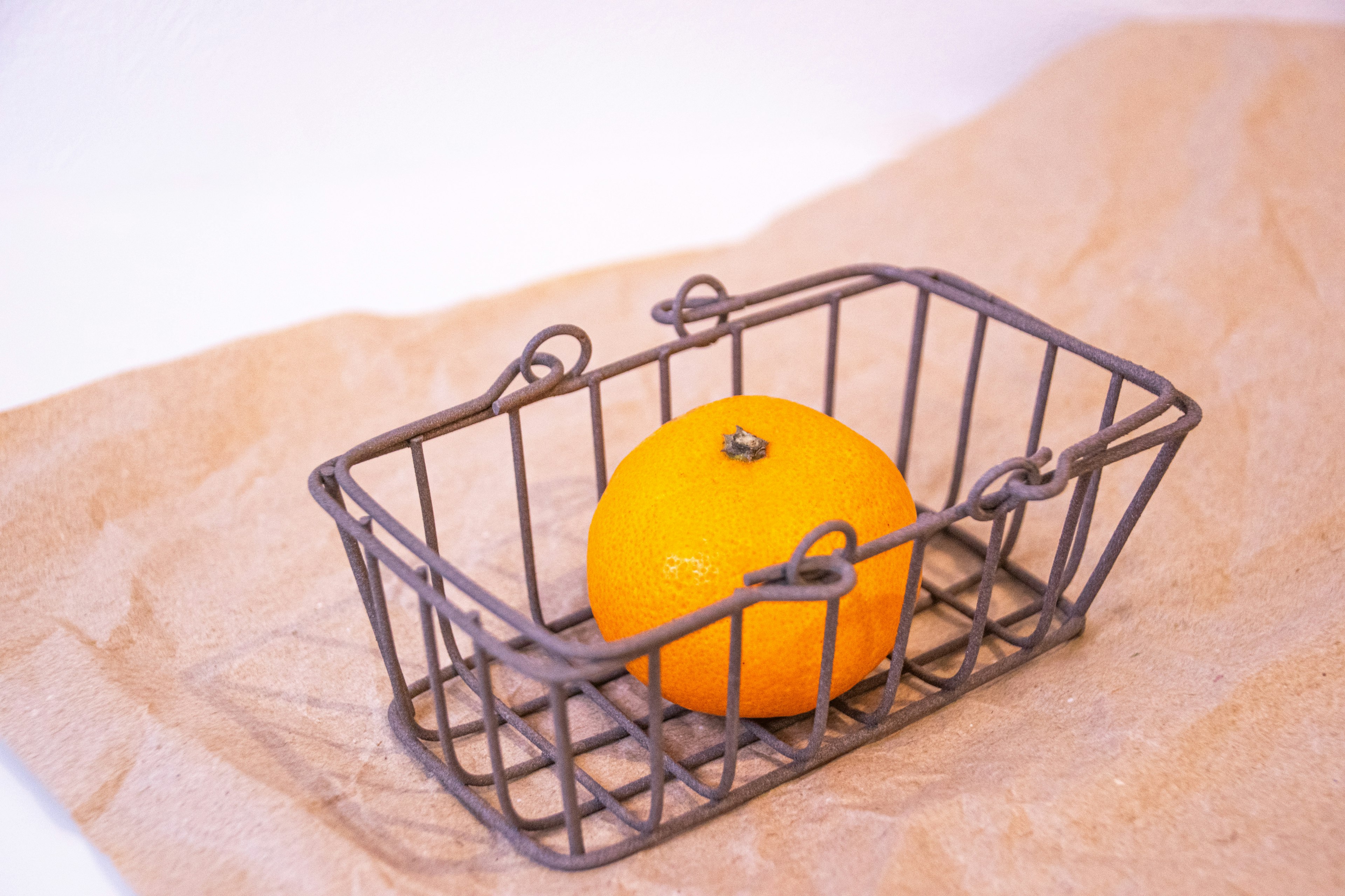 A metal basket containing an orange placed on brown paper