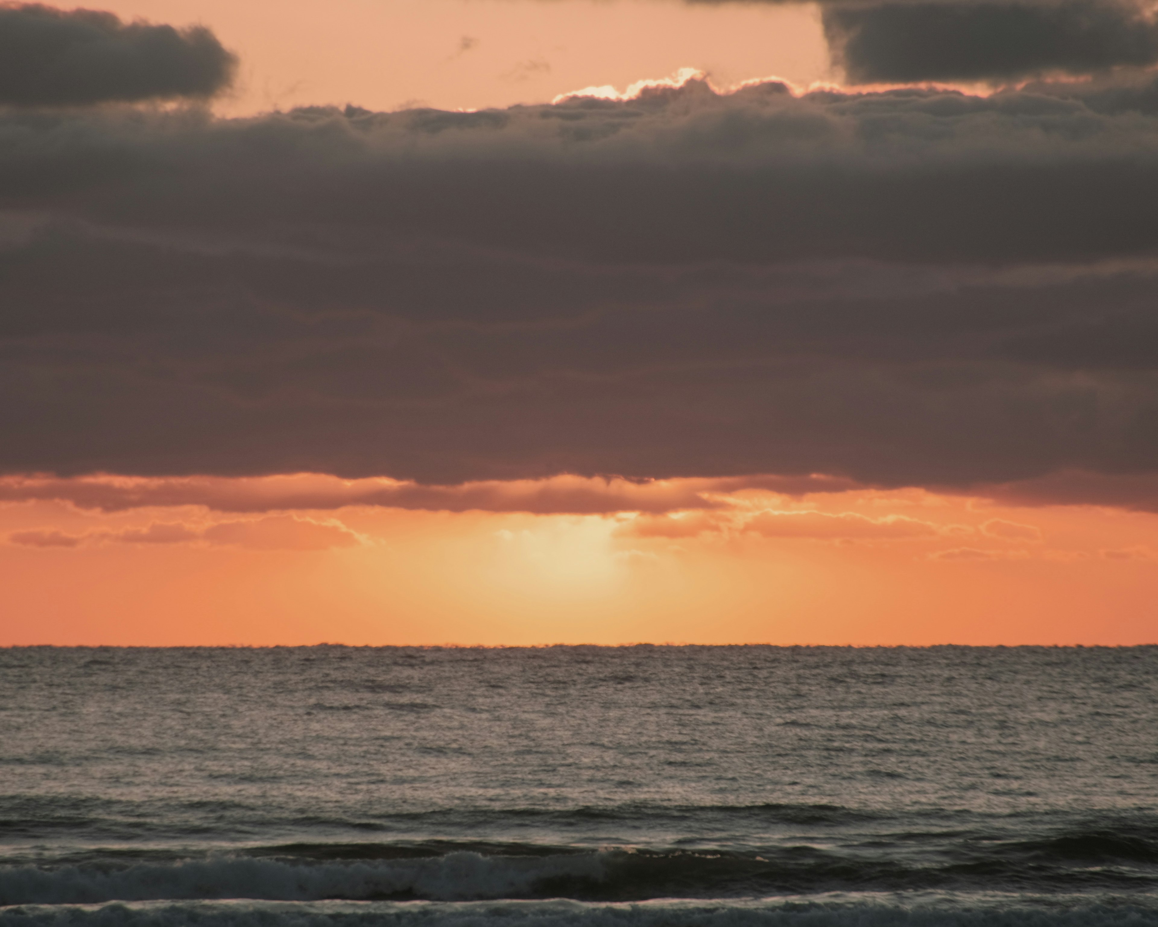 Atardecer sobre el océano con nubes y luz naranja