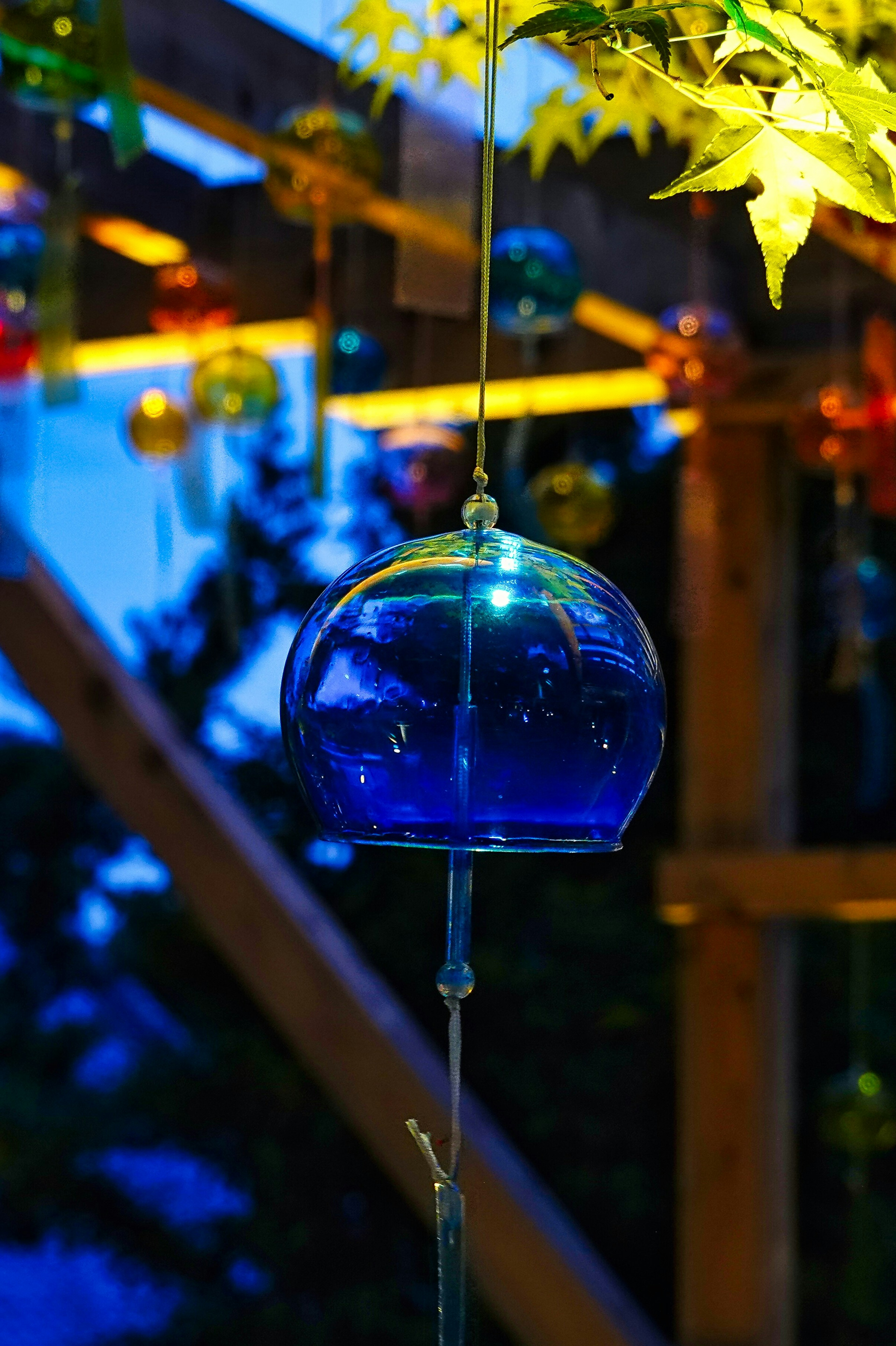 Carillón de vidrio azul colgado de una estructura de madera en un entorno nocturno