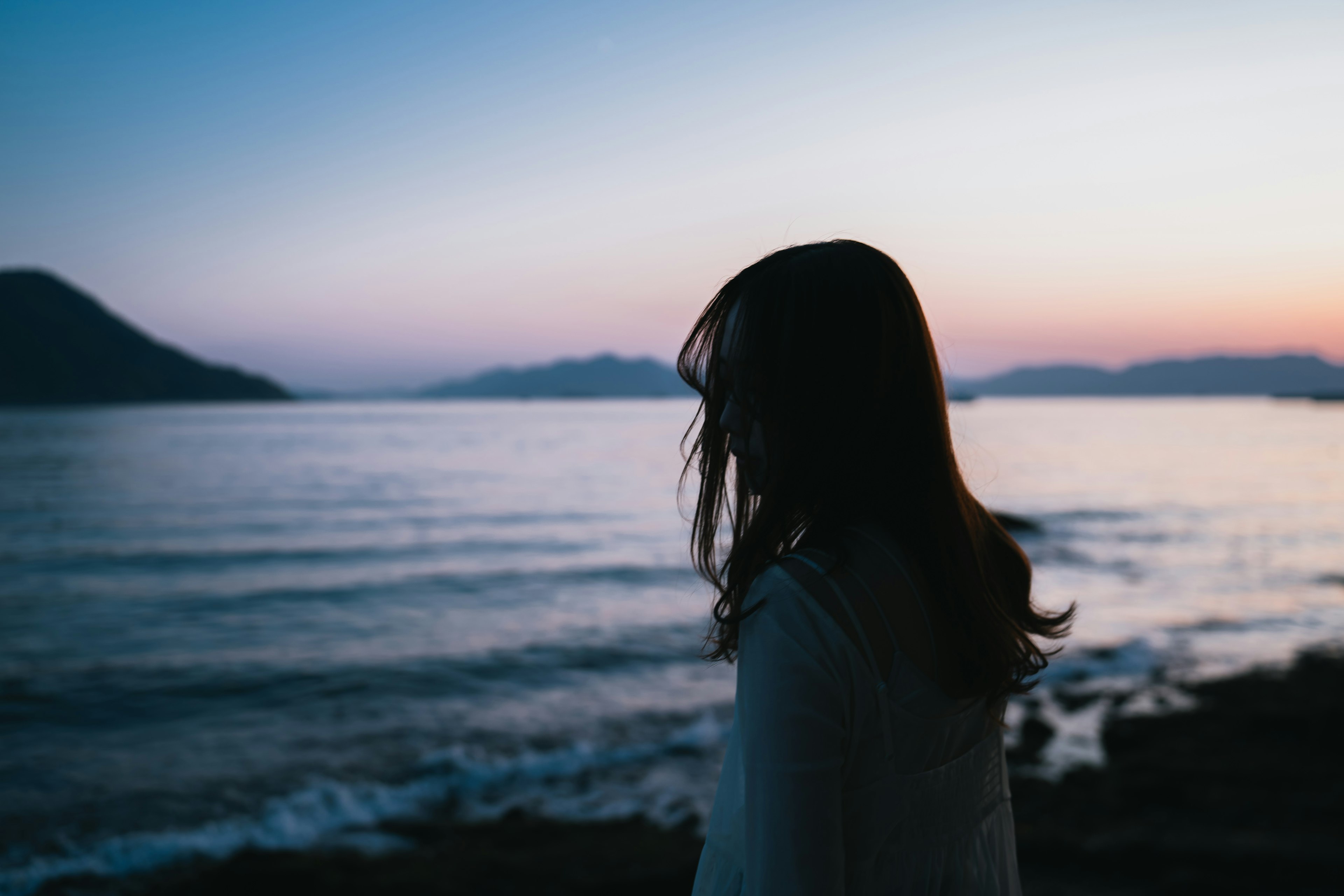 海辺で夕焼けを見つめる女性のシルエット