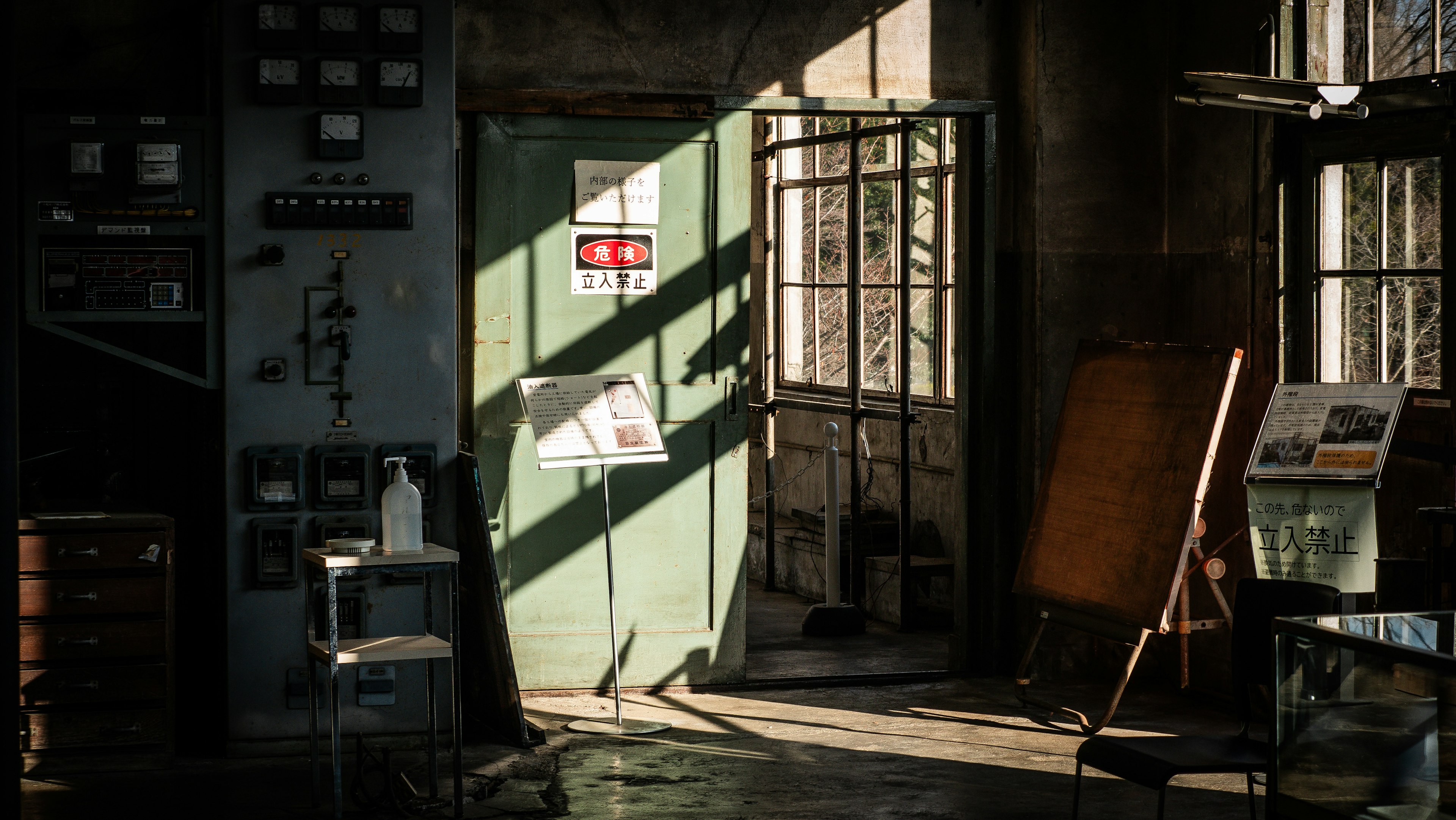 Interior de una antigua fábrica con una puerta verde y luz solar que entra por las ventanas