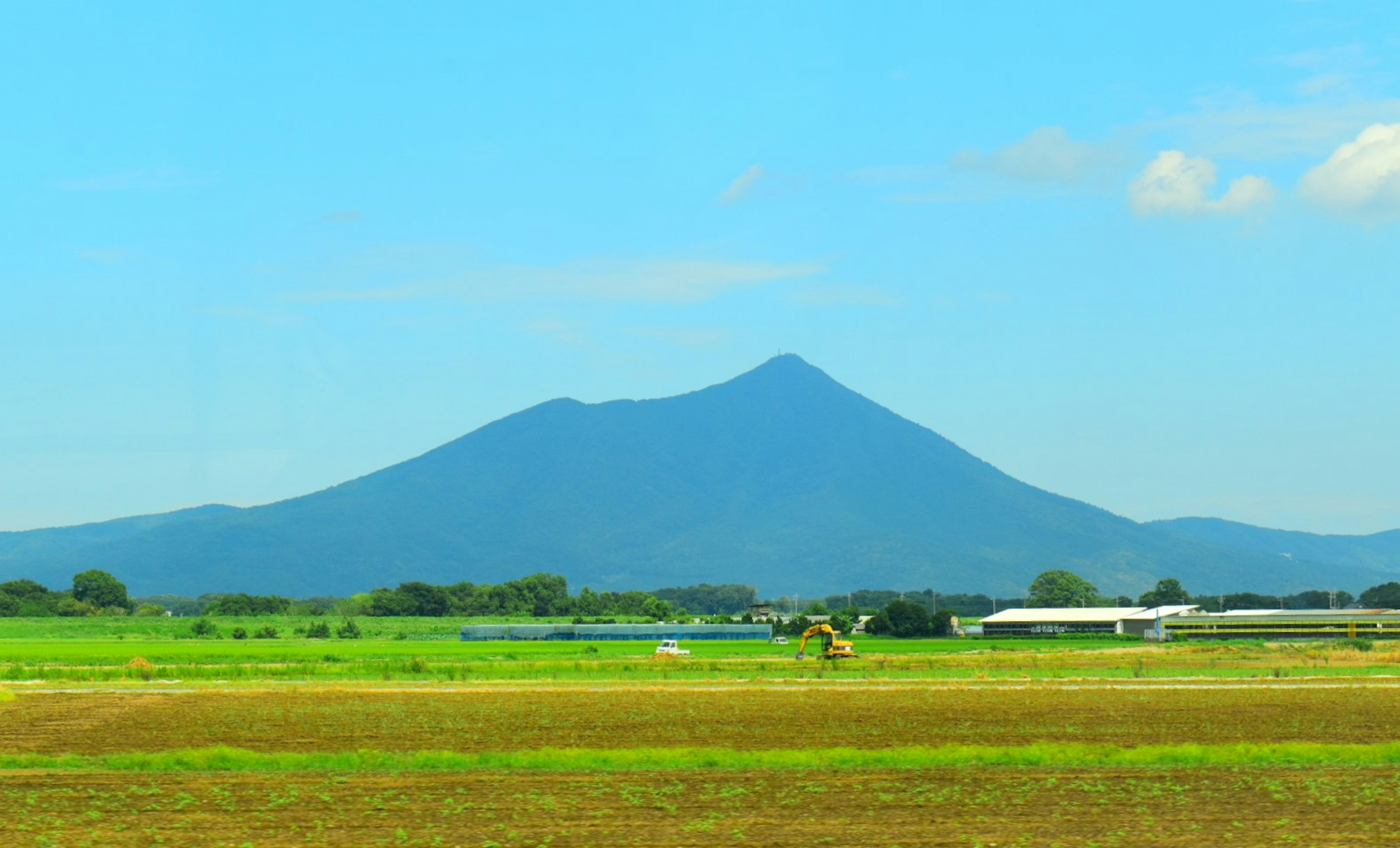 ภูเขาที่ตั้งตระหง่านใต้ท้องฟ้าสีฟ้าพร้อมทุ่งนา