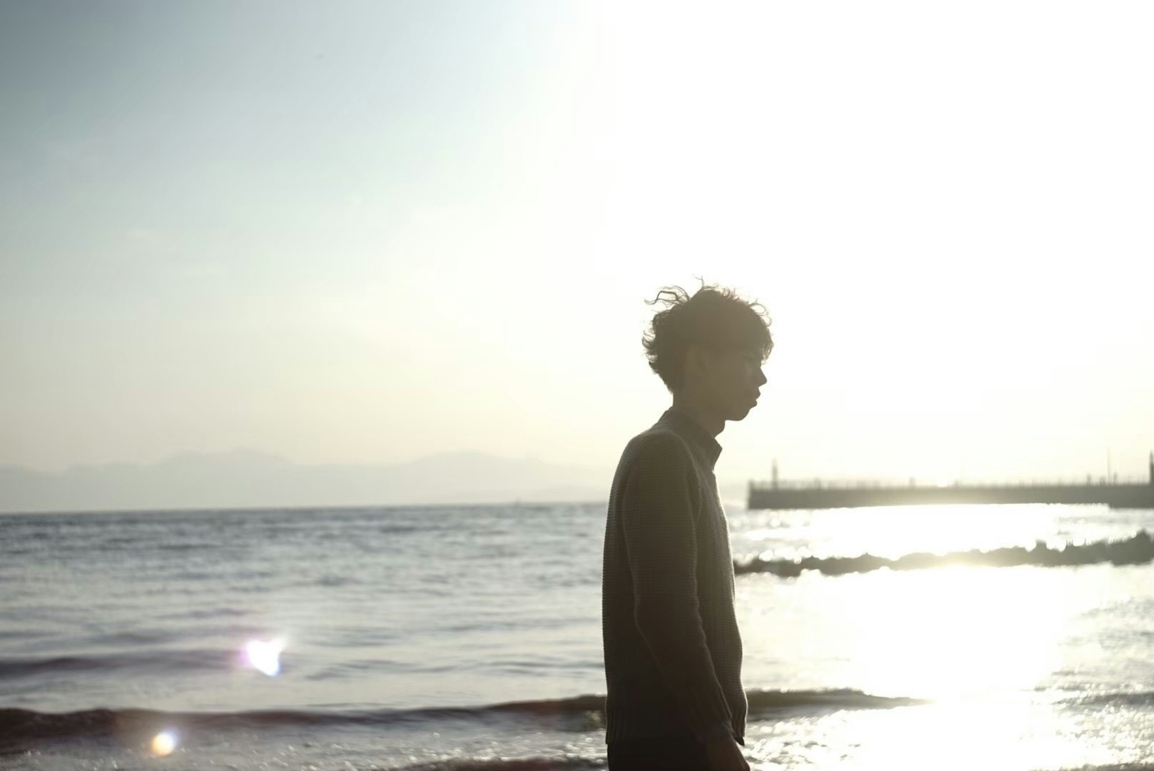 Silueta de un joven junto al mar contra el atardecer