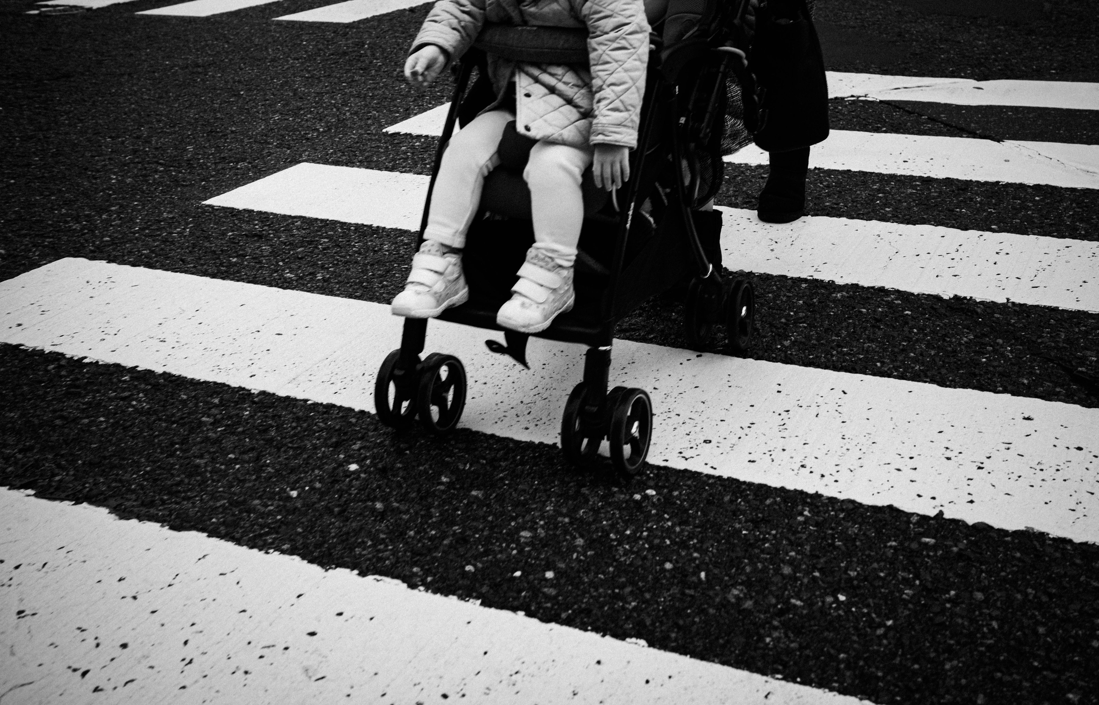 Black and white image of a stroller crossing a pedestrian crosswalk with a child's feet