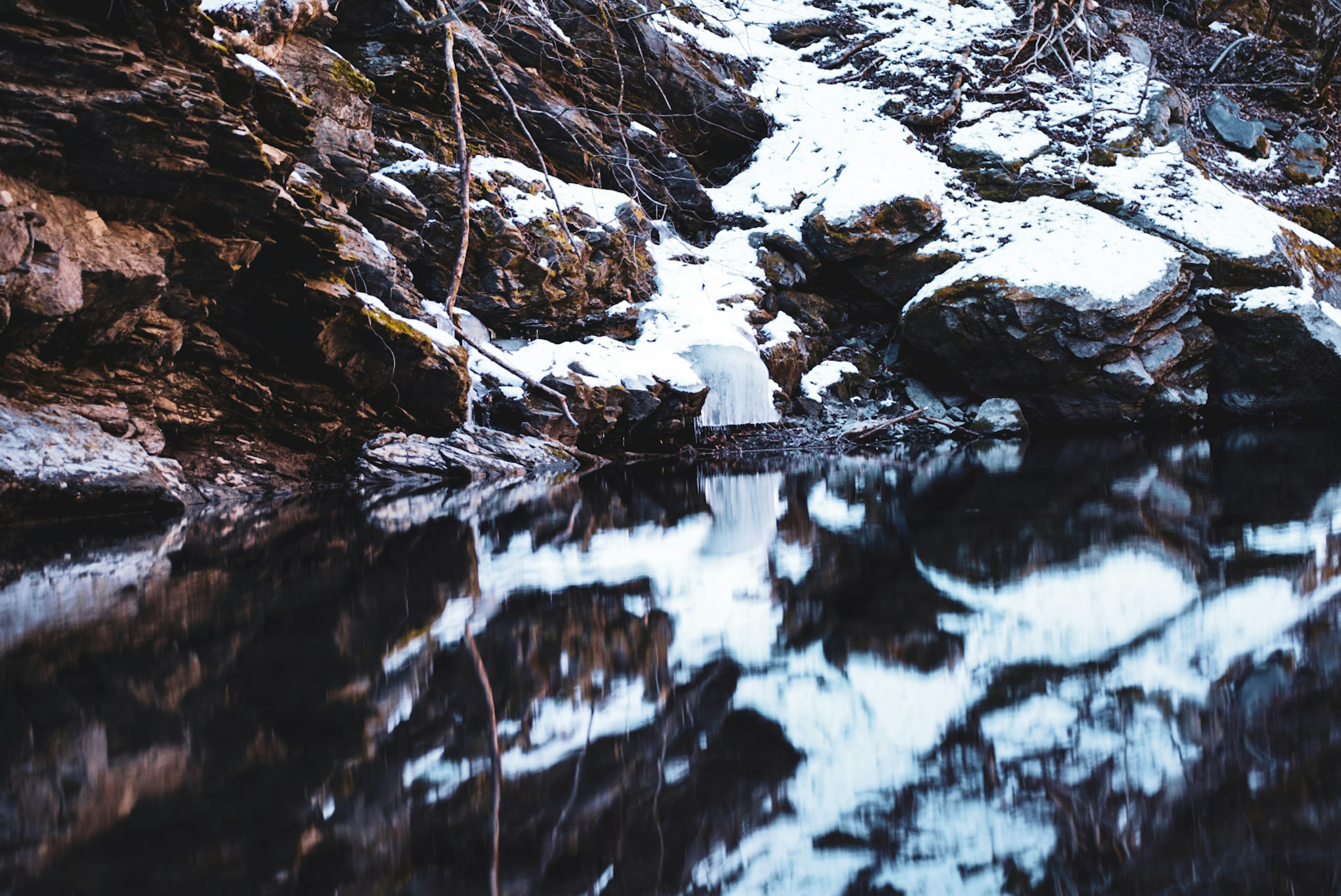 雪に覆われた岩と水面の反射が見える冬の風景