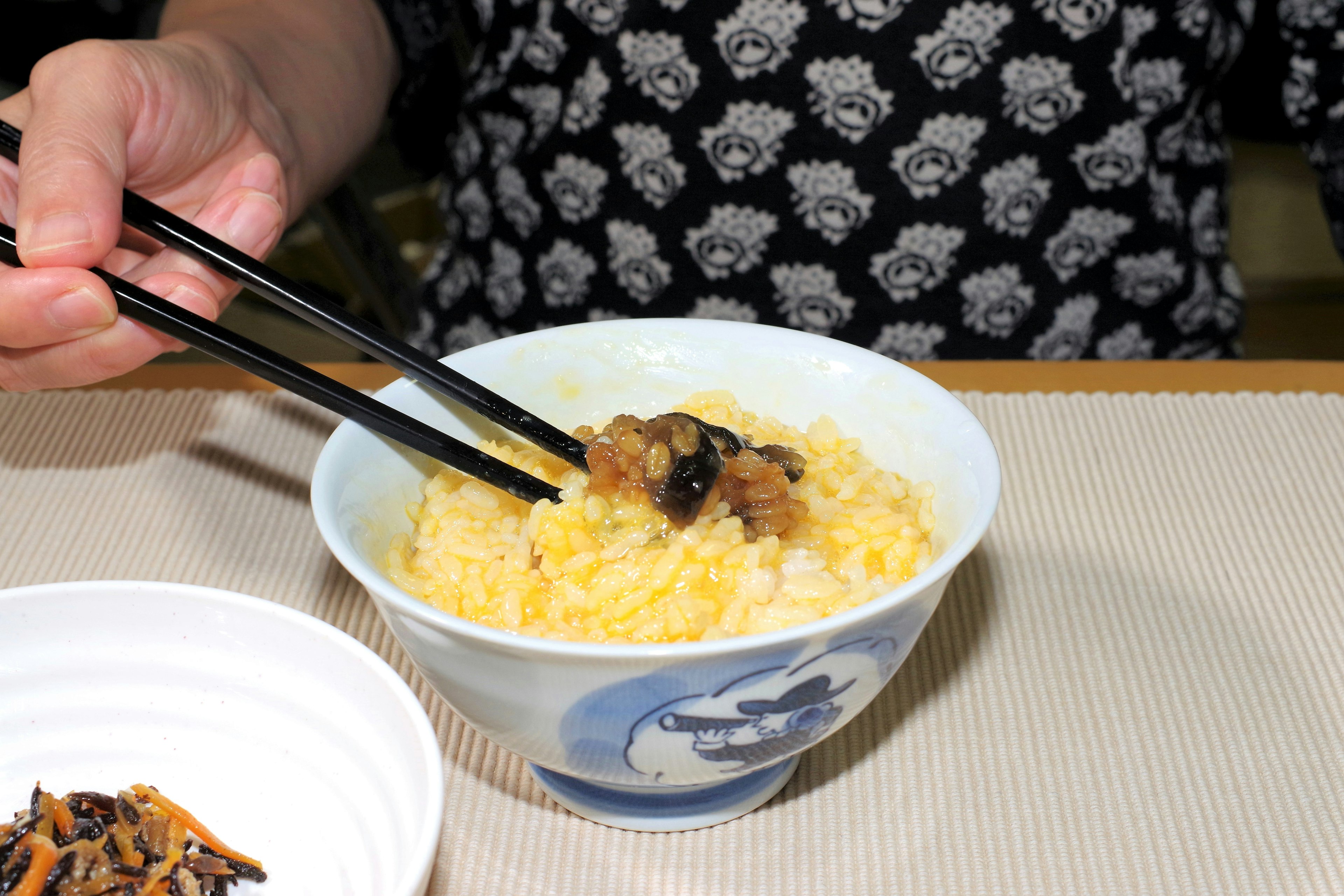 Hand holding chopsticks over a bowl of rice with toppings