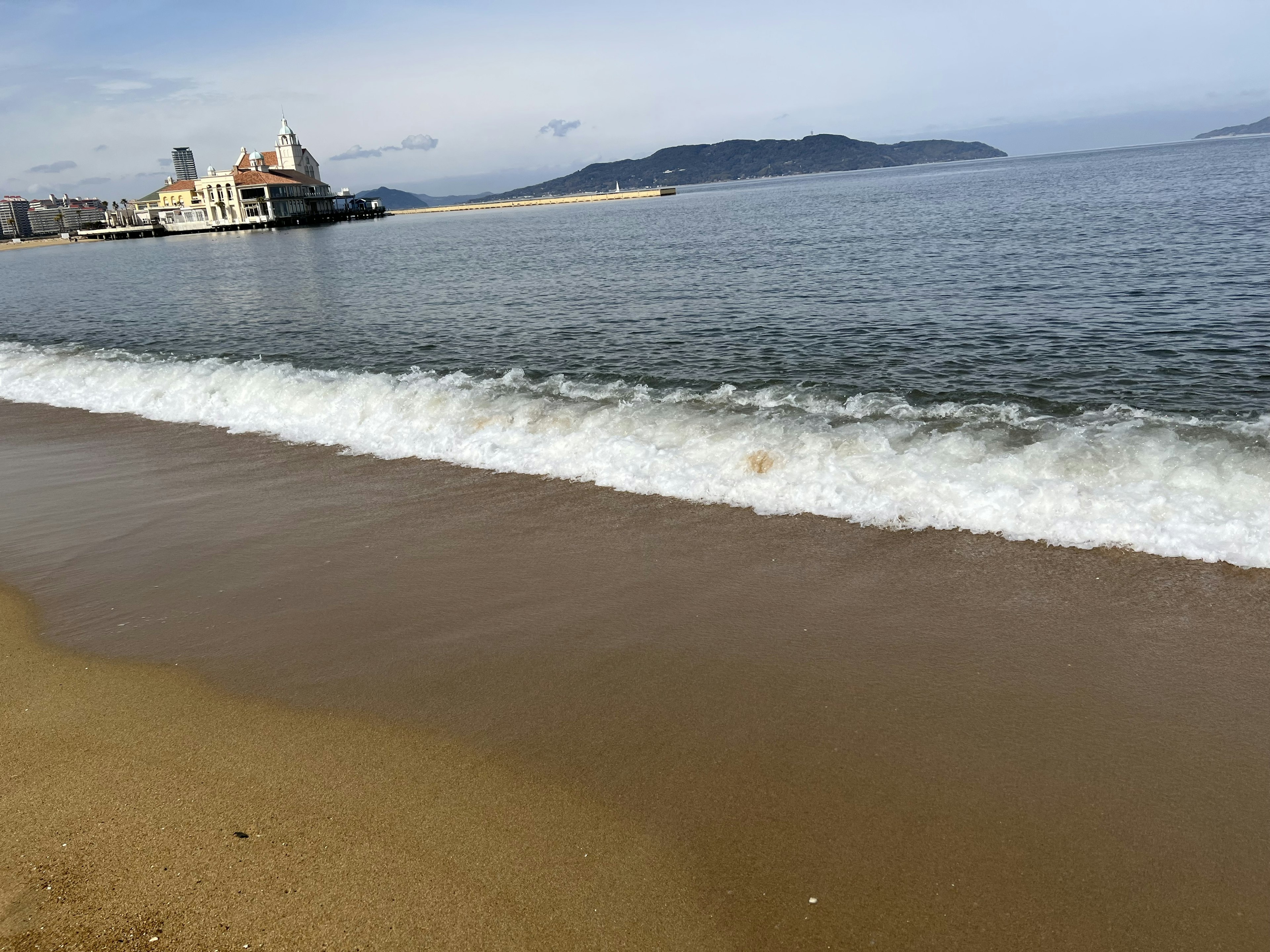 Sandy beach with waves lapping and calm sea in the background featuring buildings and mountains