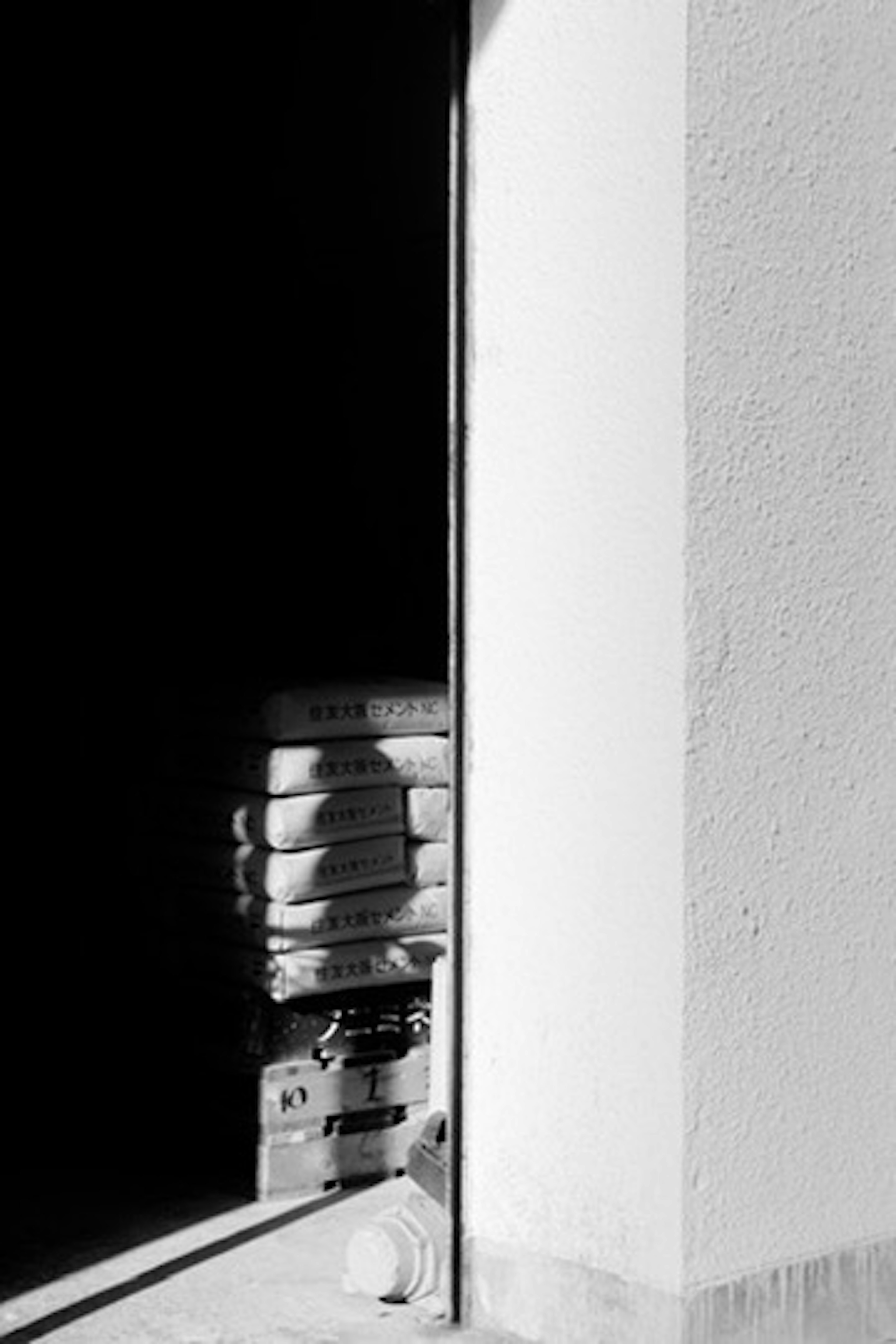 Black and white image showing stacked bags in a doorway with a dark background