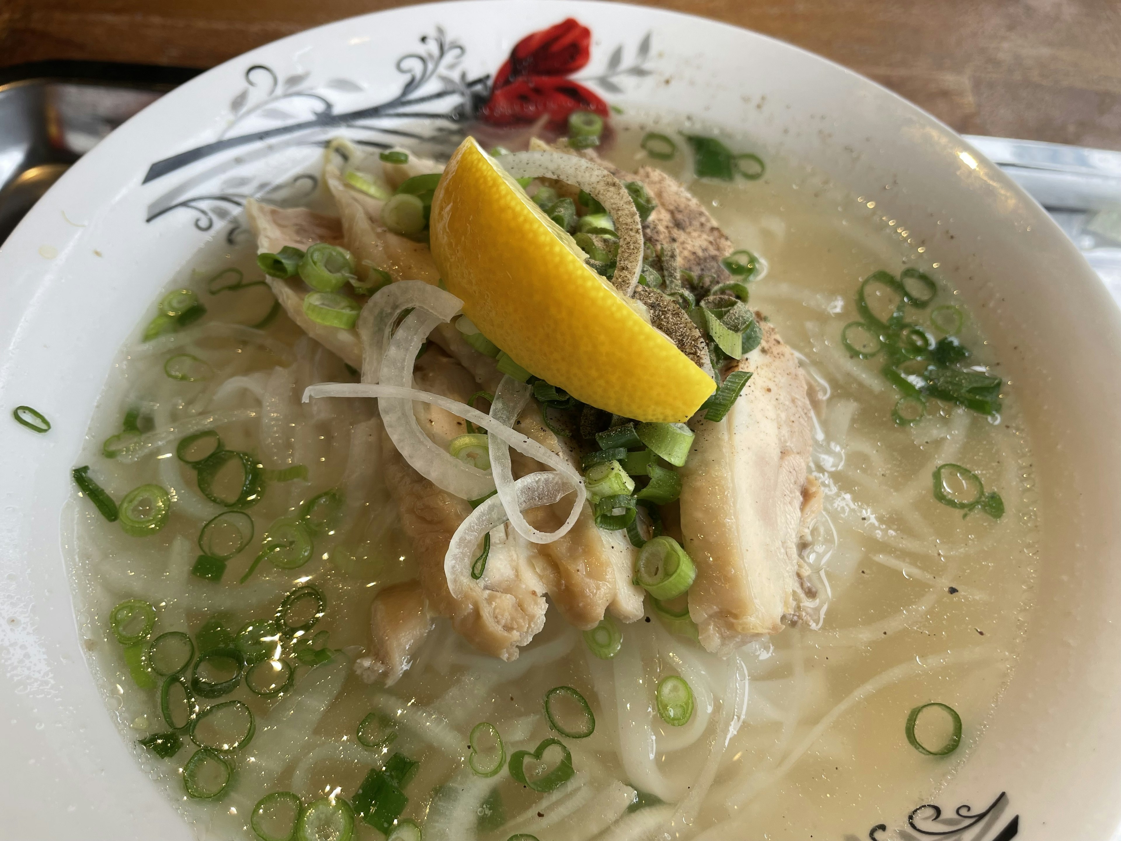 Ciotola di zuppa di pollo guarnita con cipollotti e una fetta di limone