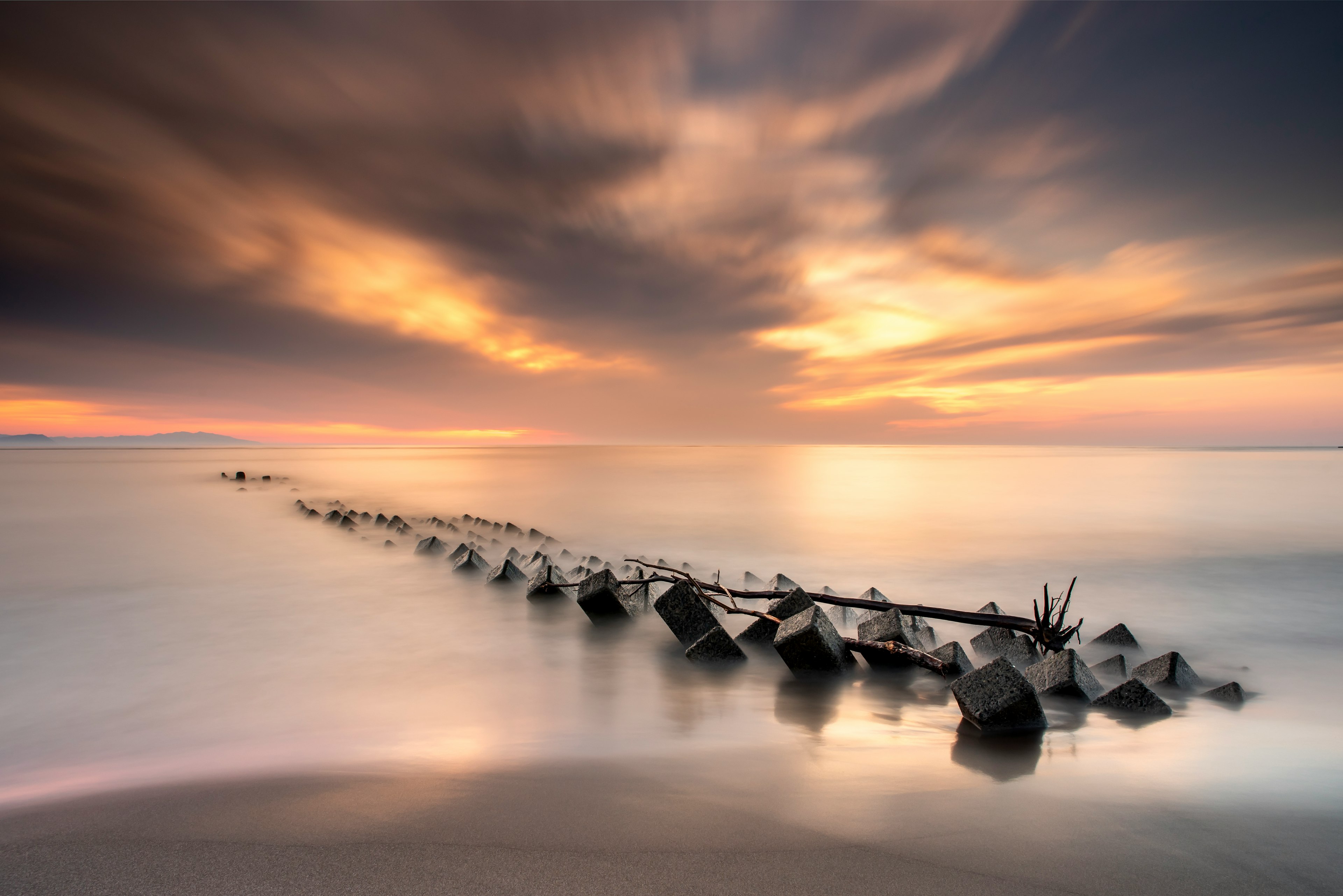 Paesaggio marino tranquillo con un sole che tramonta e un molo di pietra che si estende nell'acqua