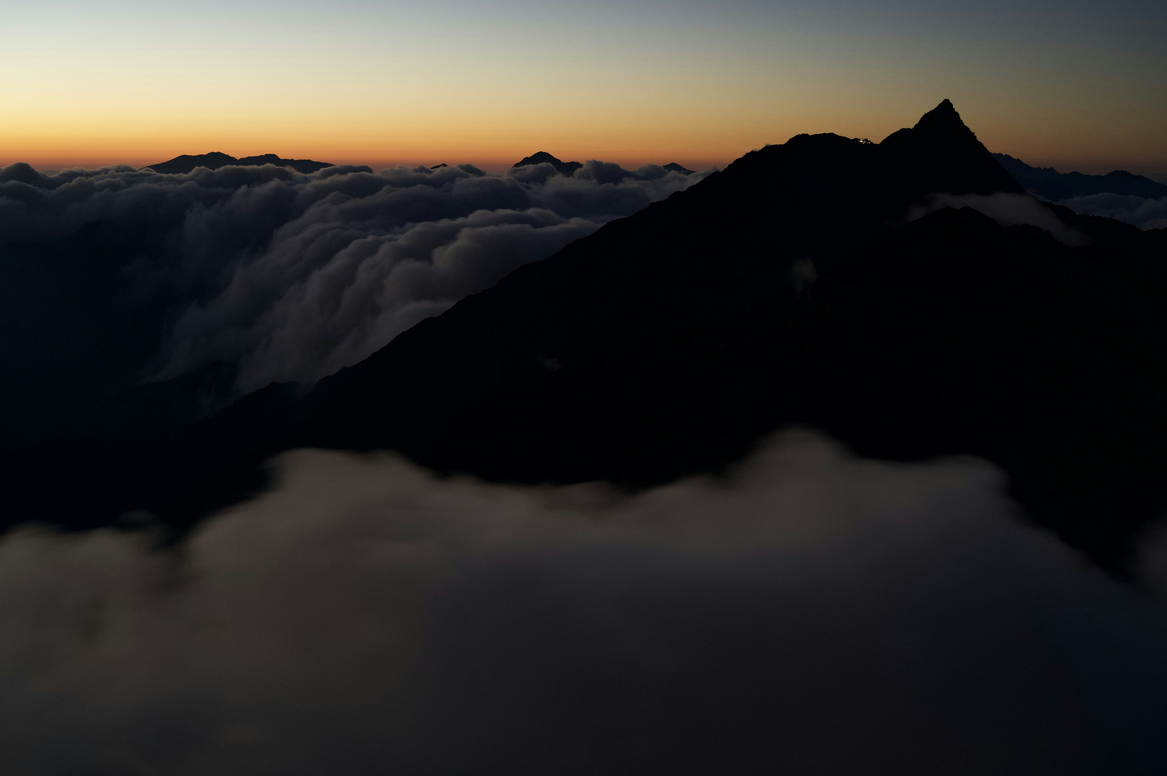 Silhouette di una montagna sopra un mare di nuvole con cielo al tramonto