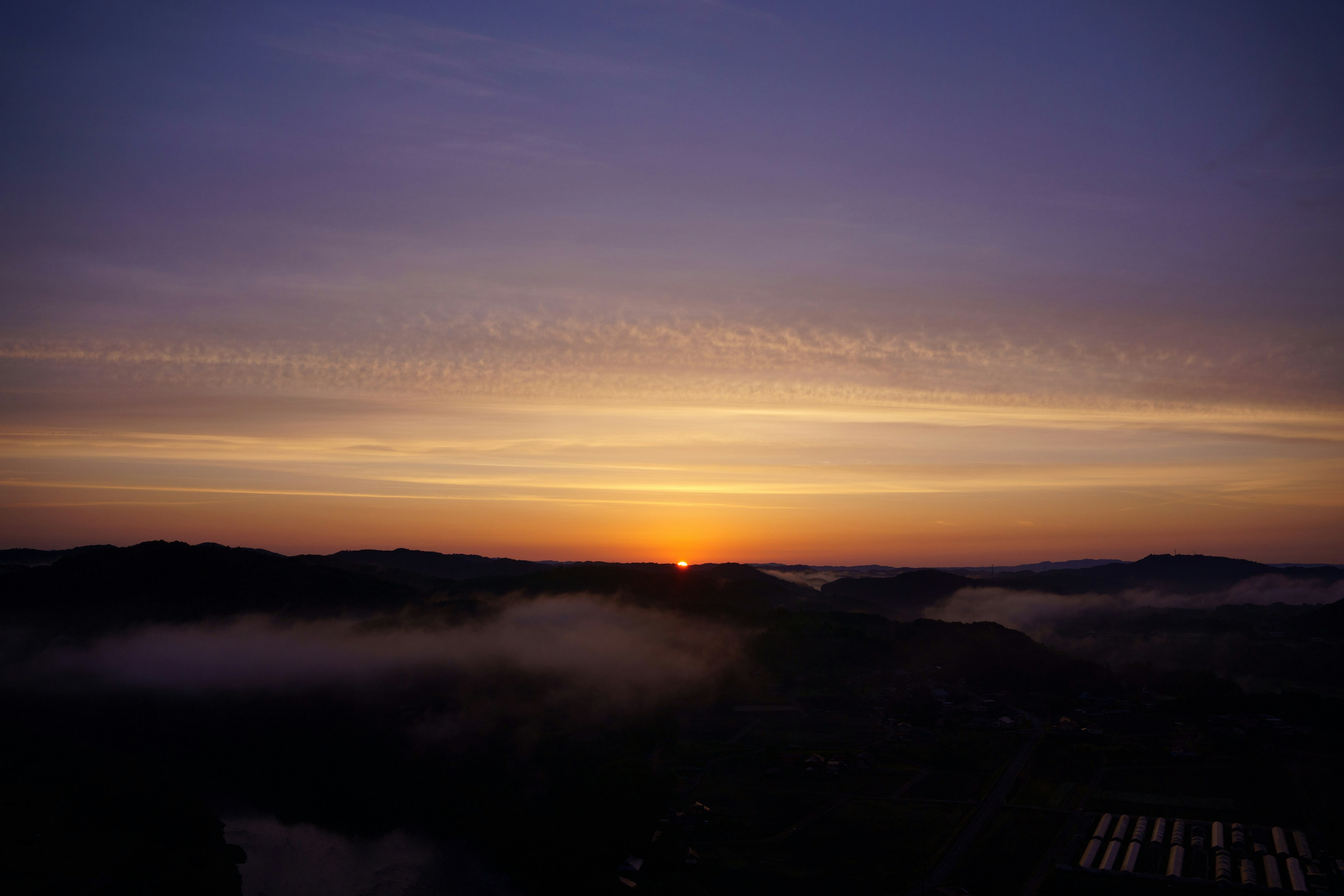 Sol naranja saliendo entre montañas bajo un cielo púrpura con nubes delgadas