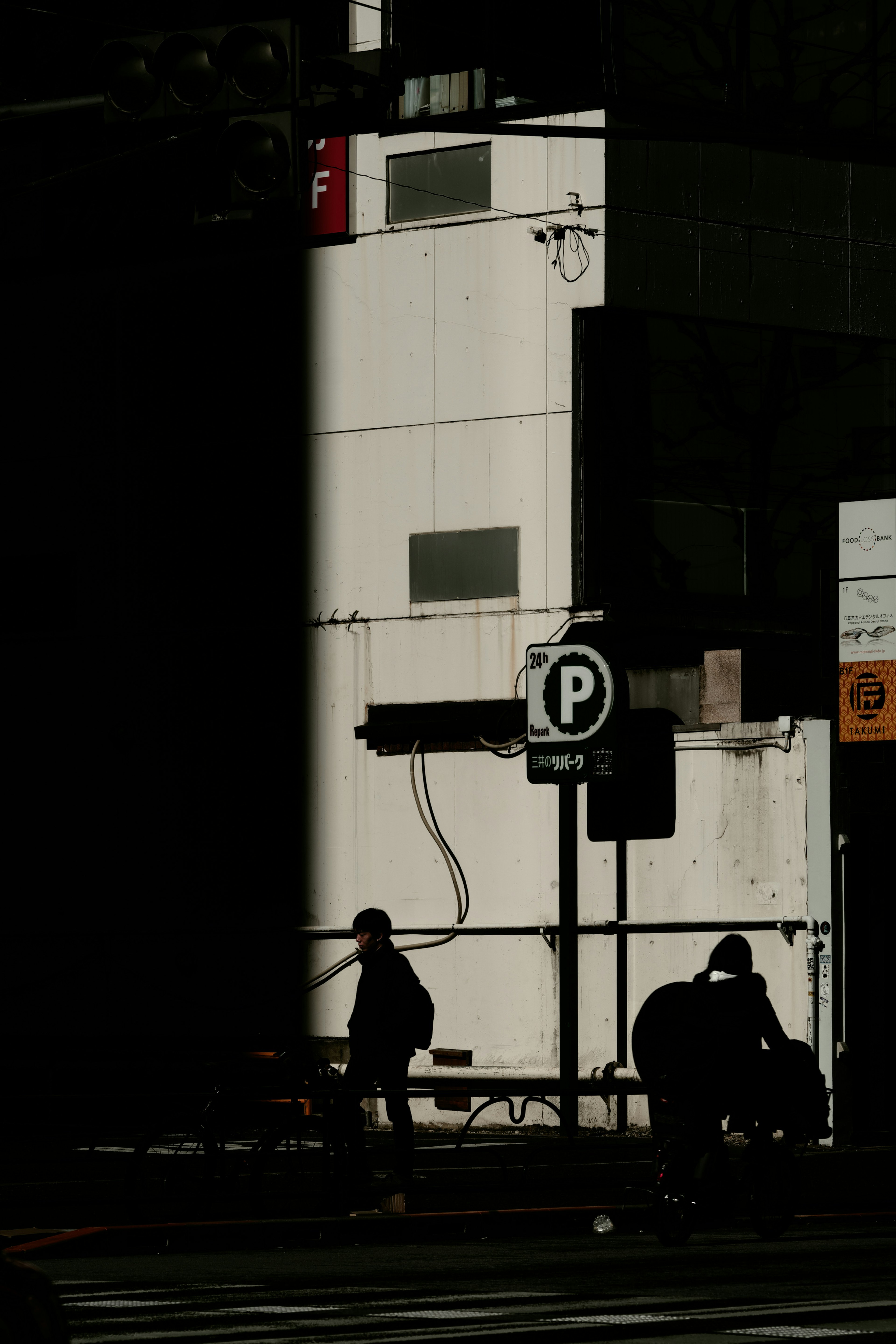 Urban scene featuring shadows and a white wall with pedestrians