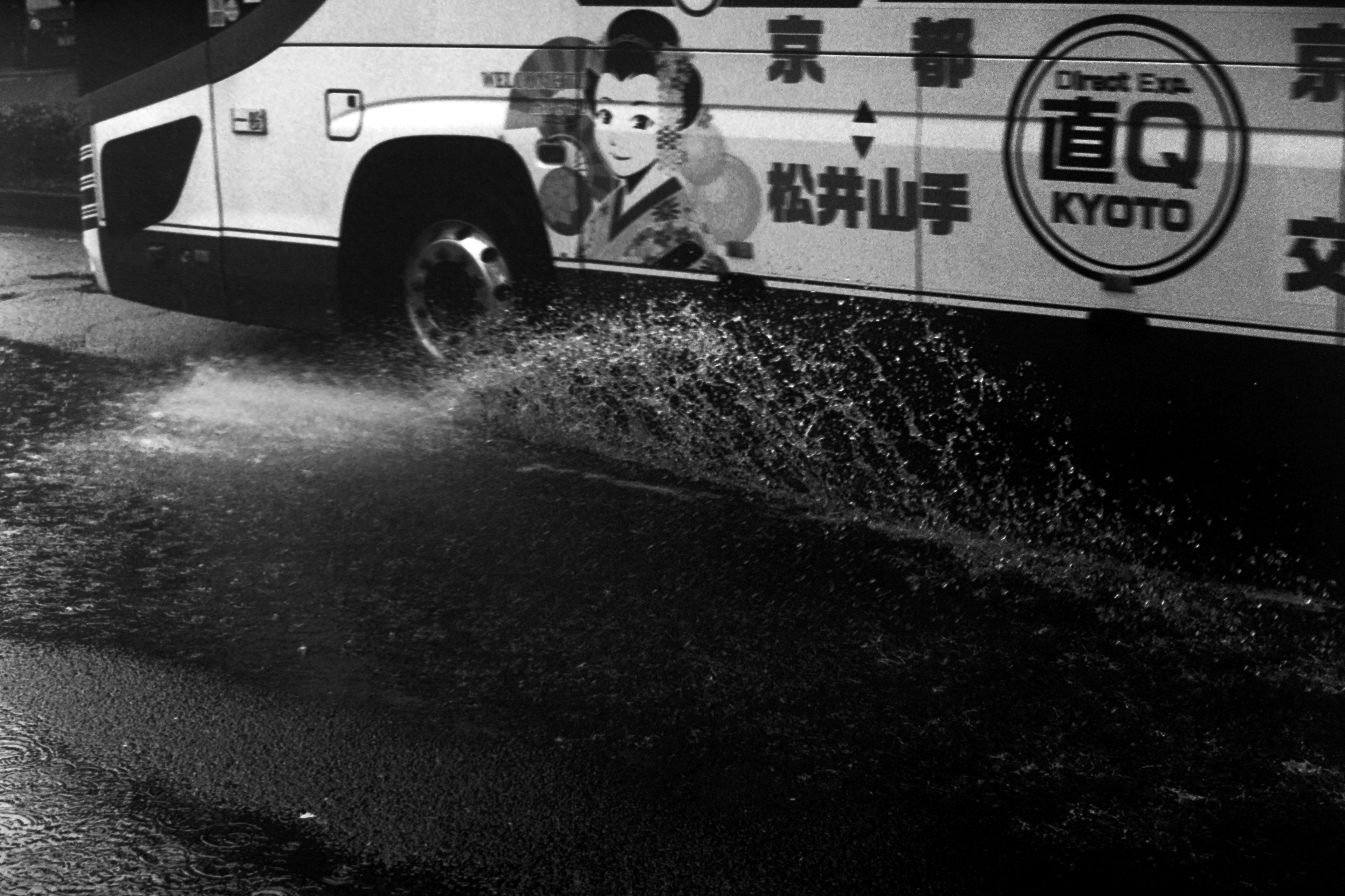 Foto hitam putih bus melewati genangan air di malam hari di Kyoto