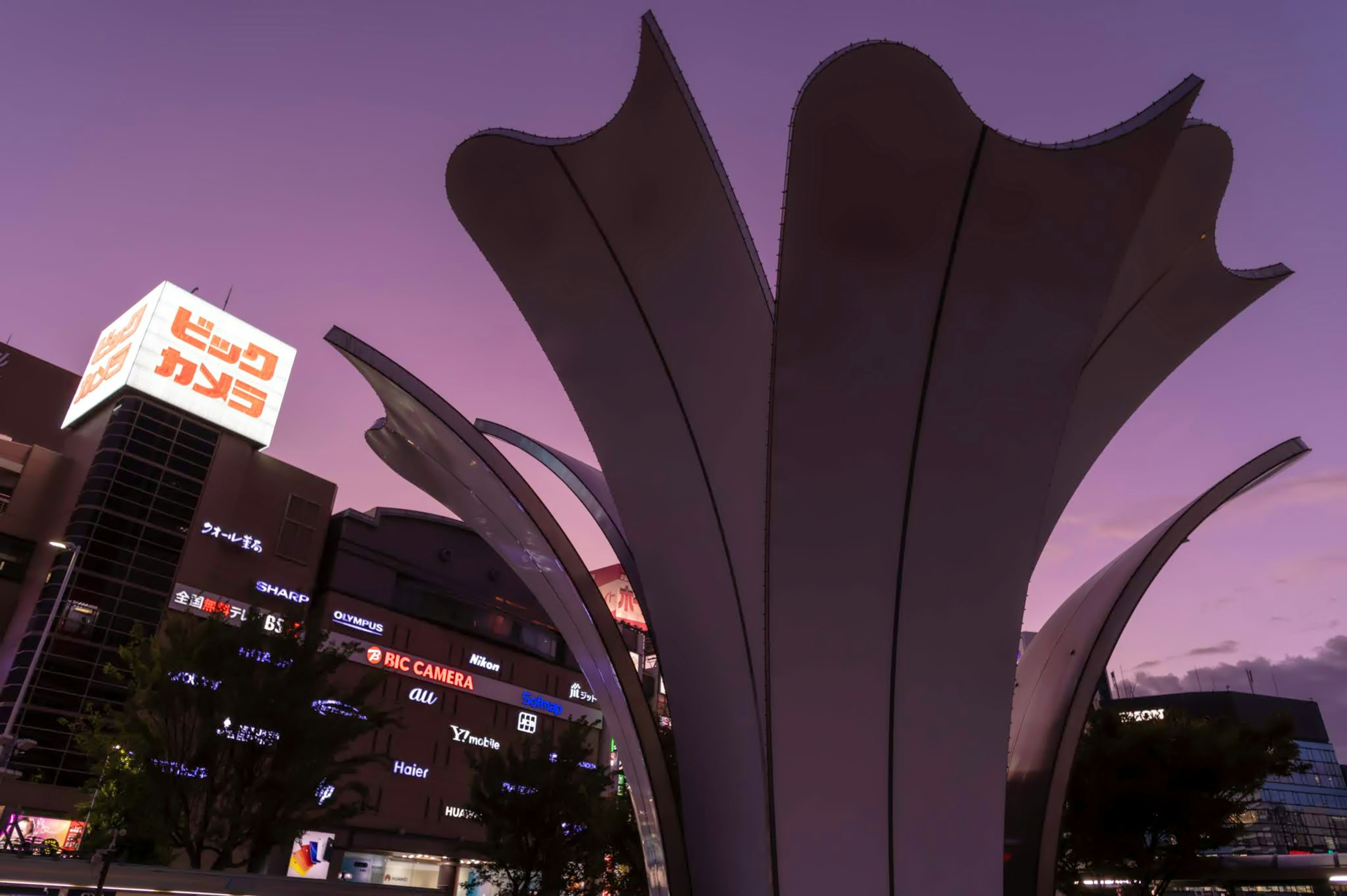 Escultura que recuerda pétalos contra un cielo crepuscular con fondo urbano