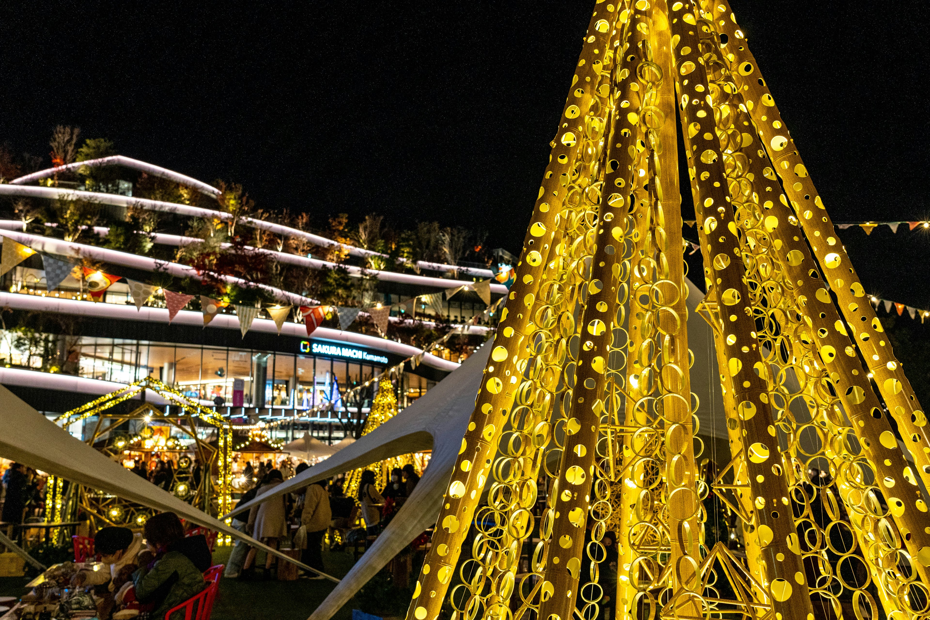 Illuminated yellow decorative Christmas tree with a building in the background at night