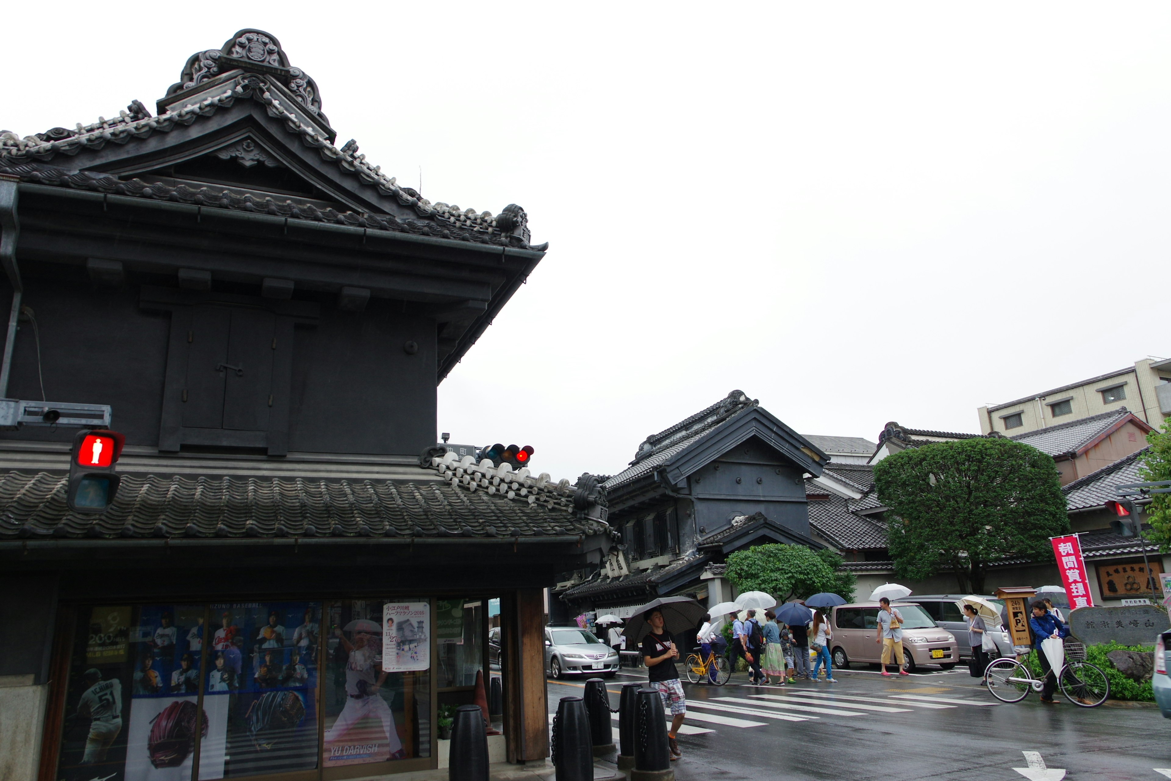 Intersección con arquitectura japonesa tradicional y edificios comerciales modernos bajo la lluvia