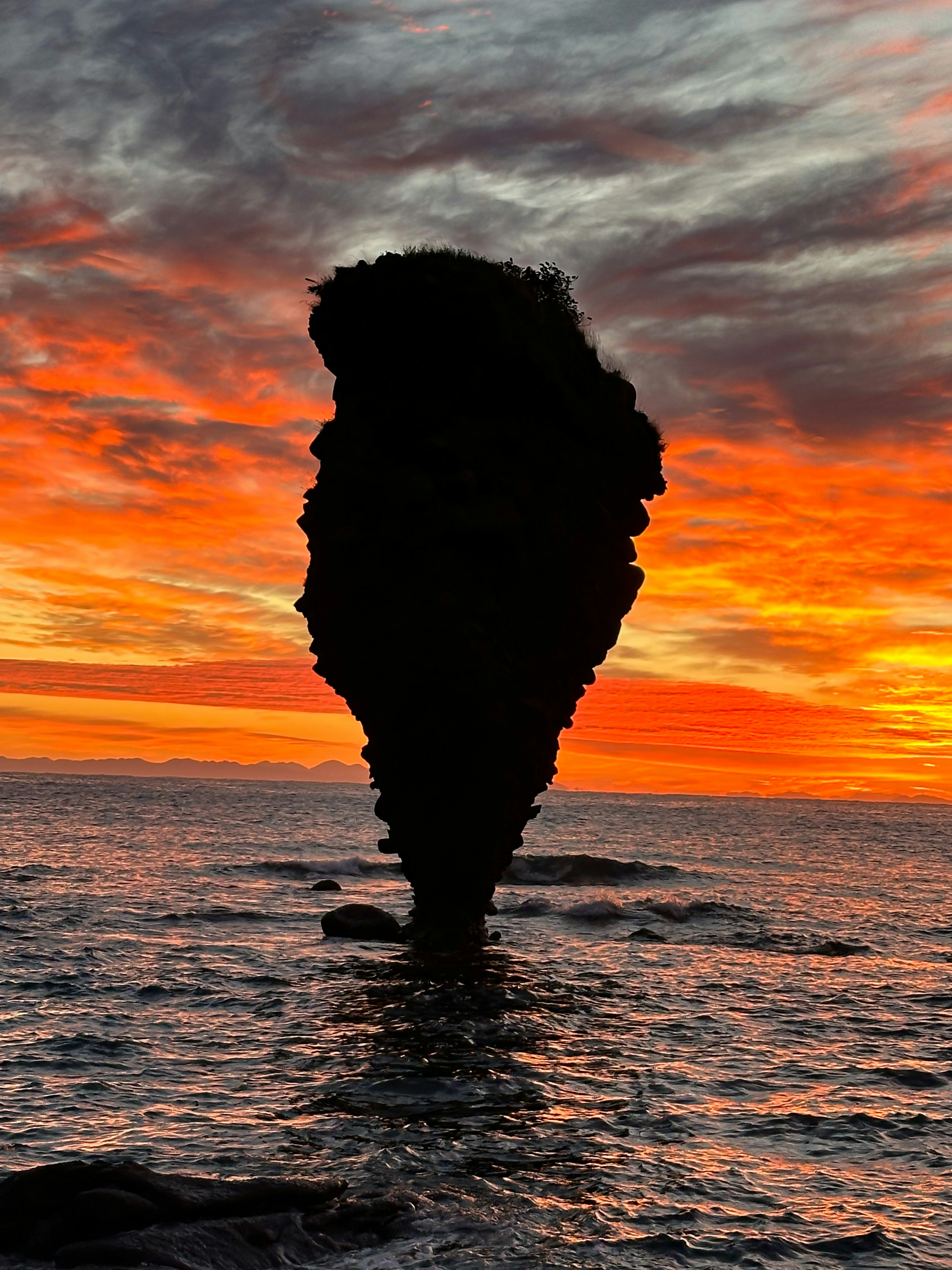 Unique rock silhouette towering in a sunset reflecting orange hues over the sea