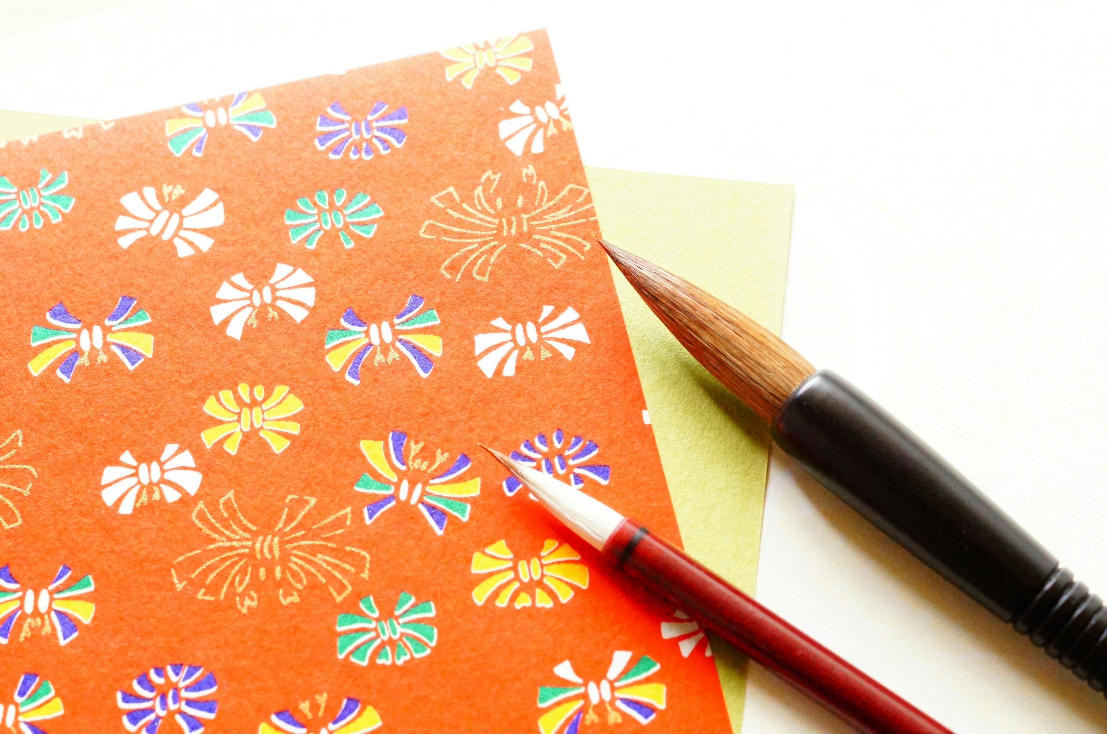 Papier orange à motifs floraux avec un pinceau un stylo rouge et du papier vert