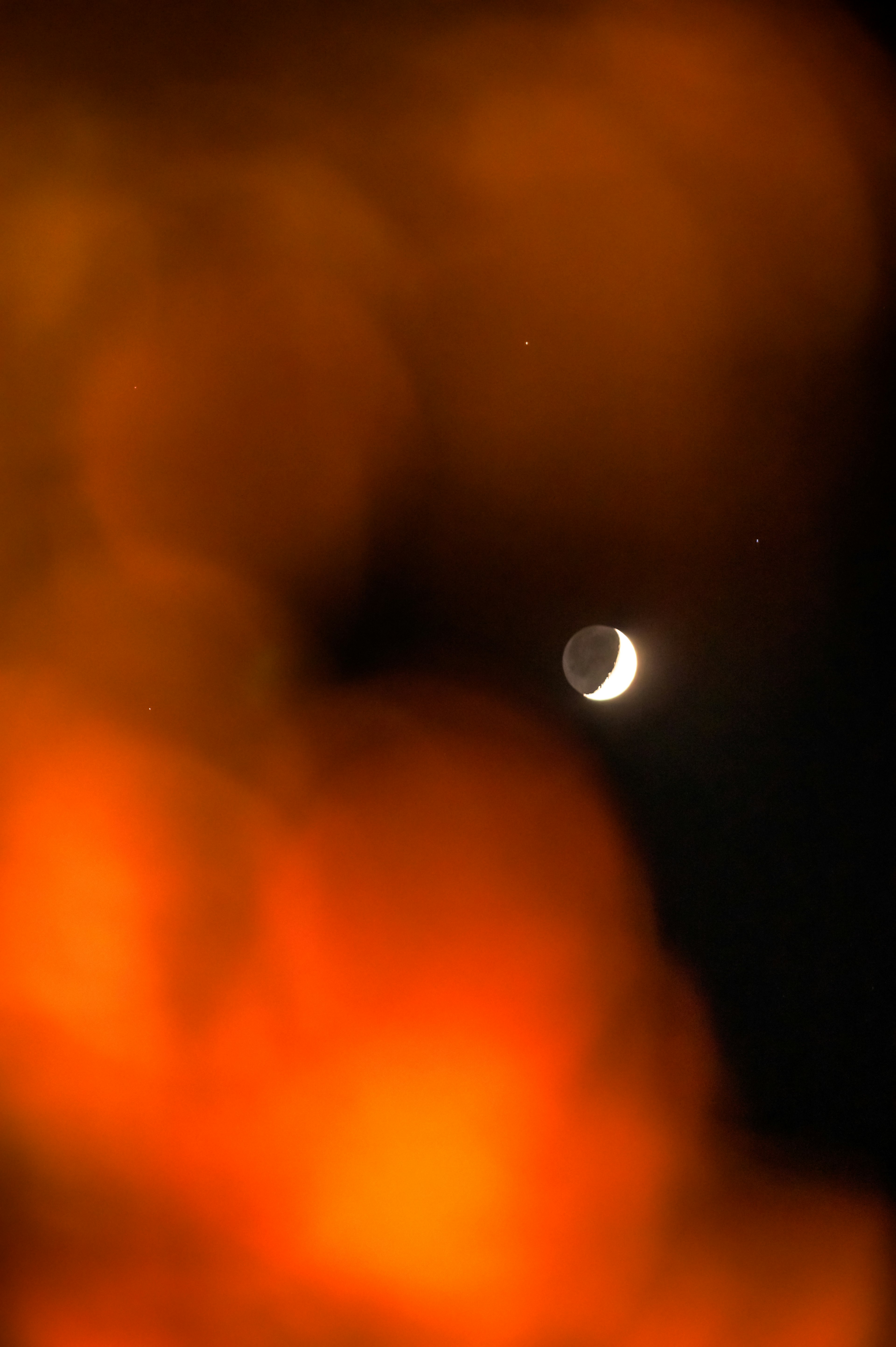 Luna creciente visible entre nubes naranjas