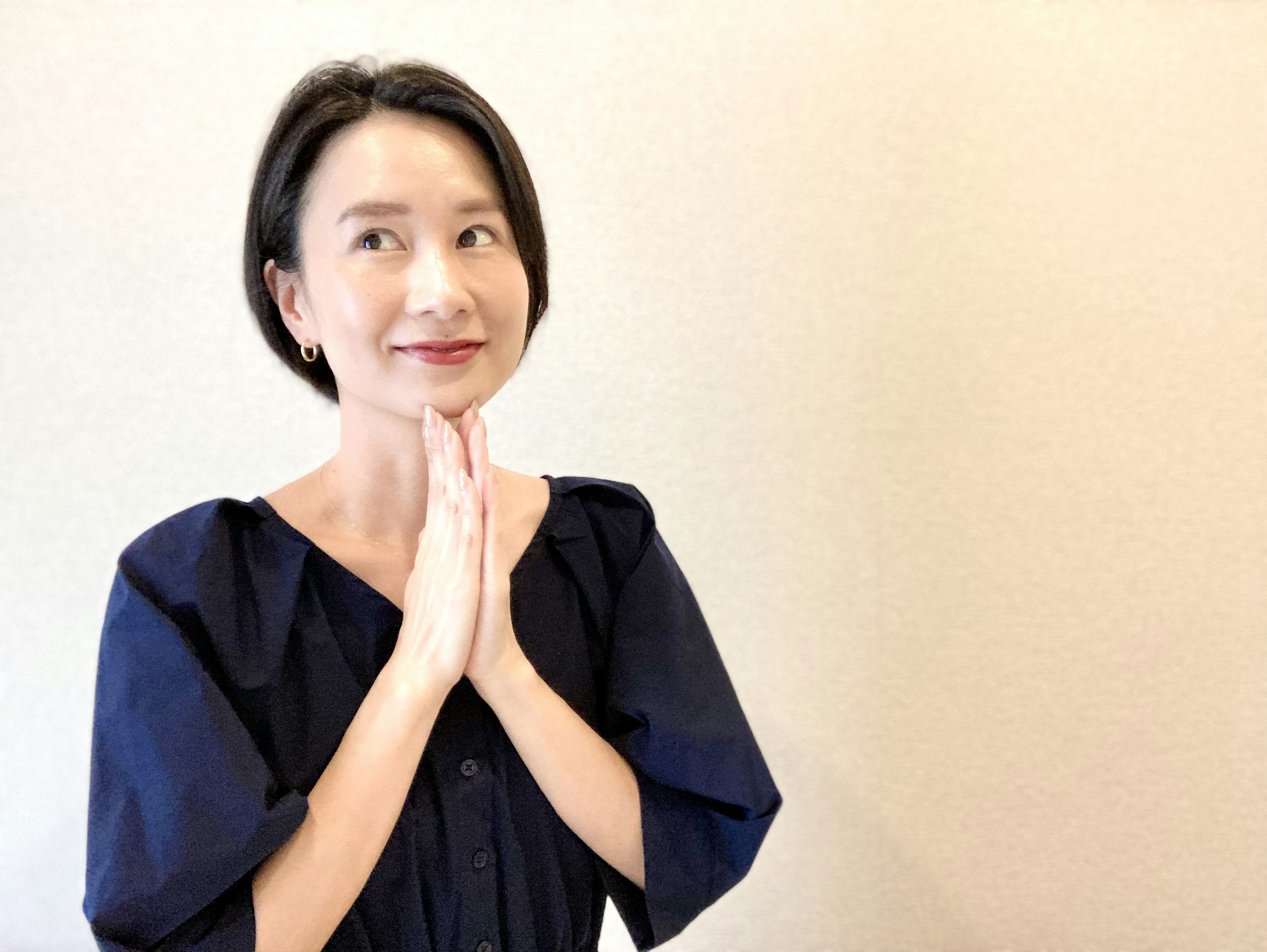 A woman in a blue outfit with hands clasped and a smile