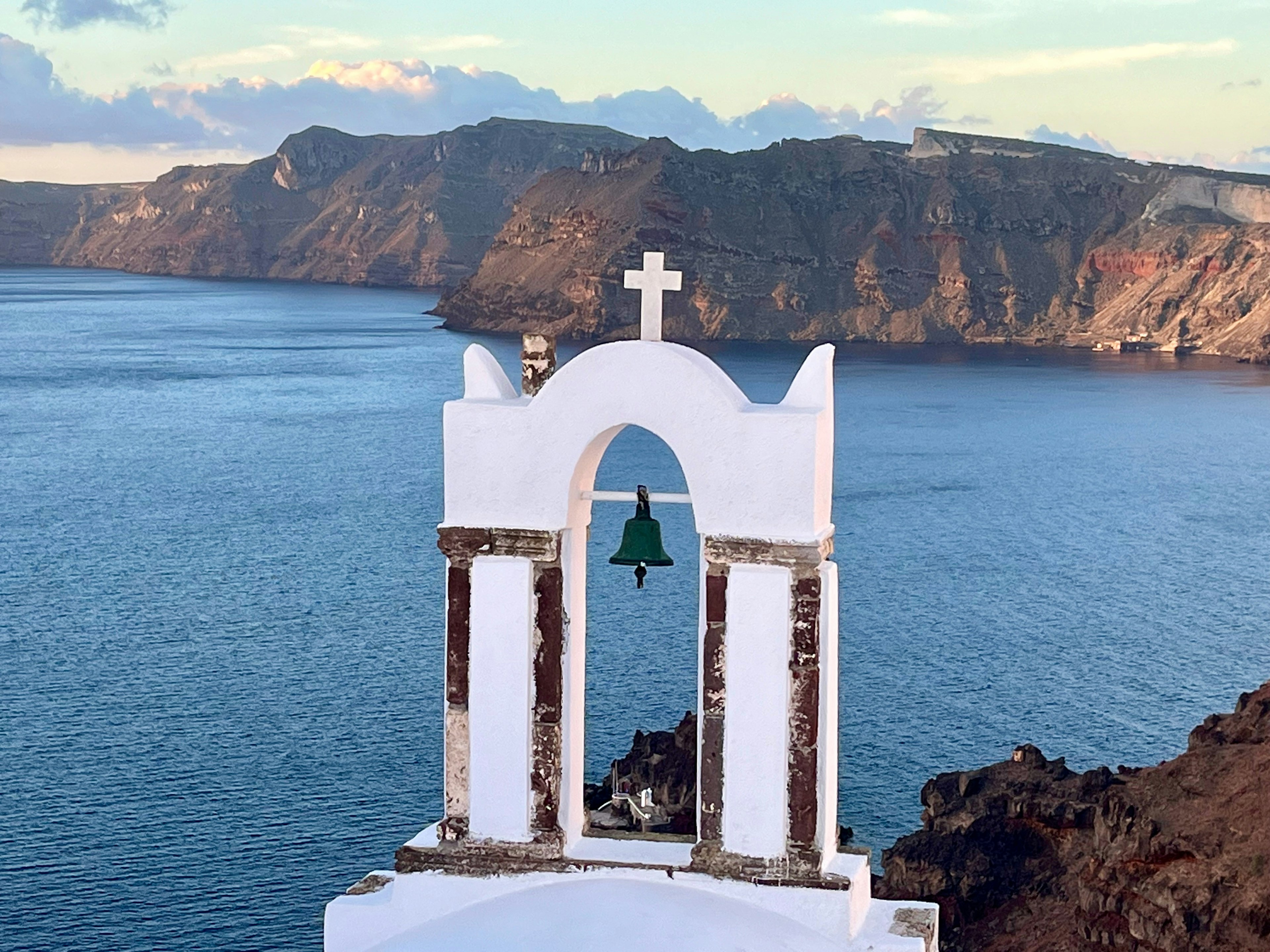 White church bell tower with a cross overlooking a blue sea