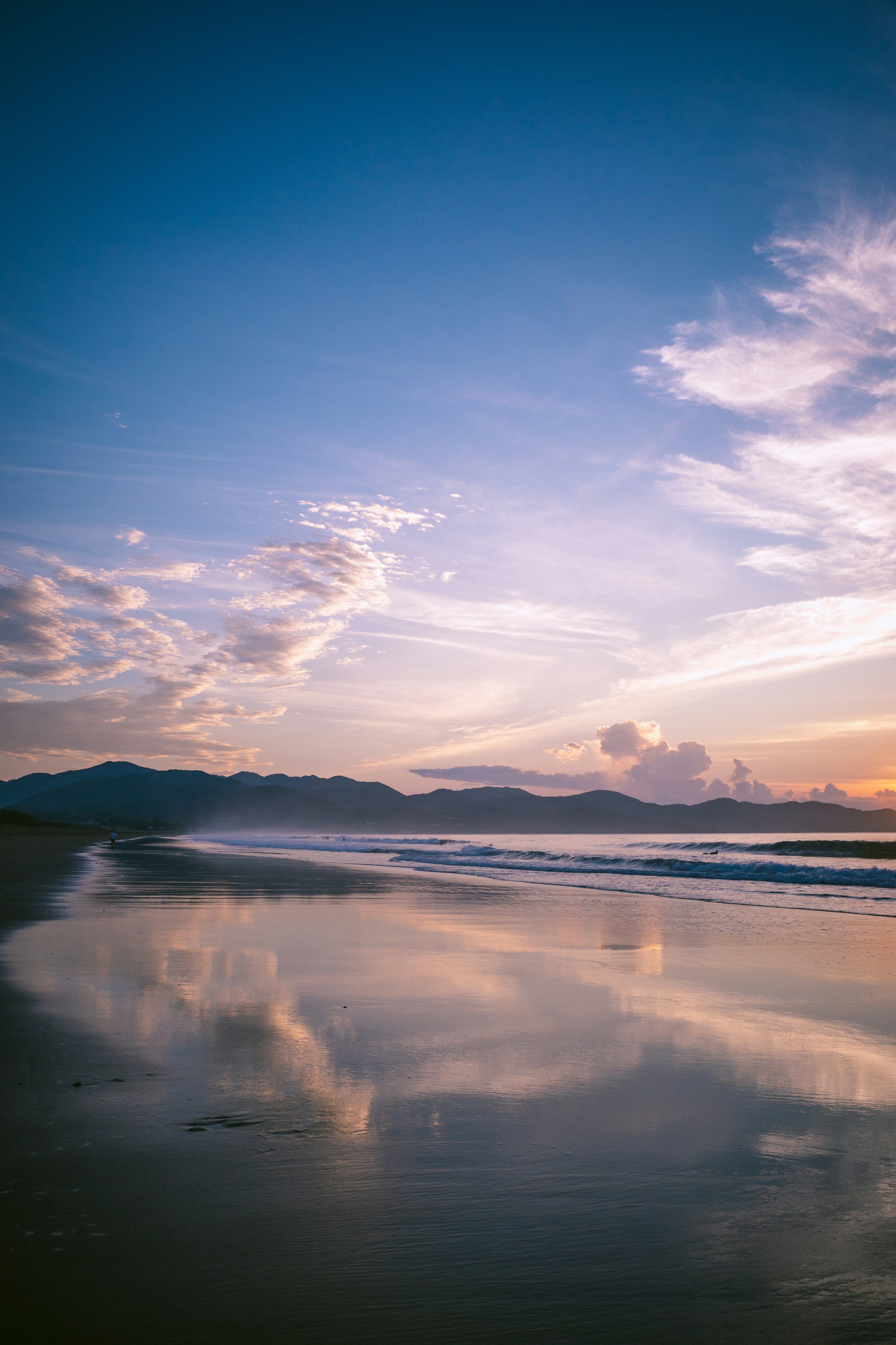 ชายหาดที่สวยงามพร้อมท้องฟ้าสีฟ้า ผิวน้ำสะท้อนและเมฆอ่อน