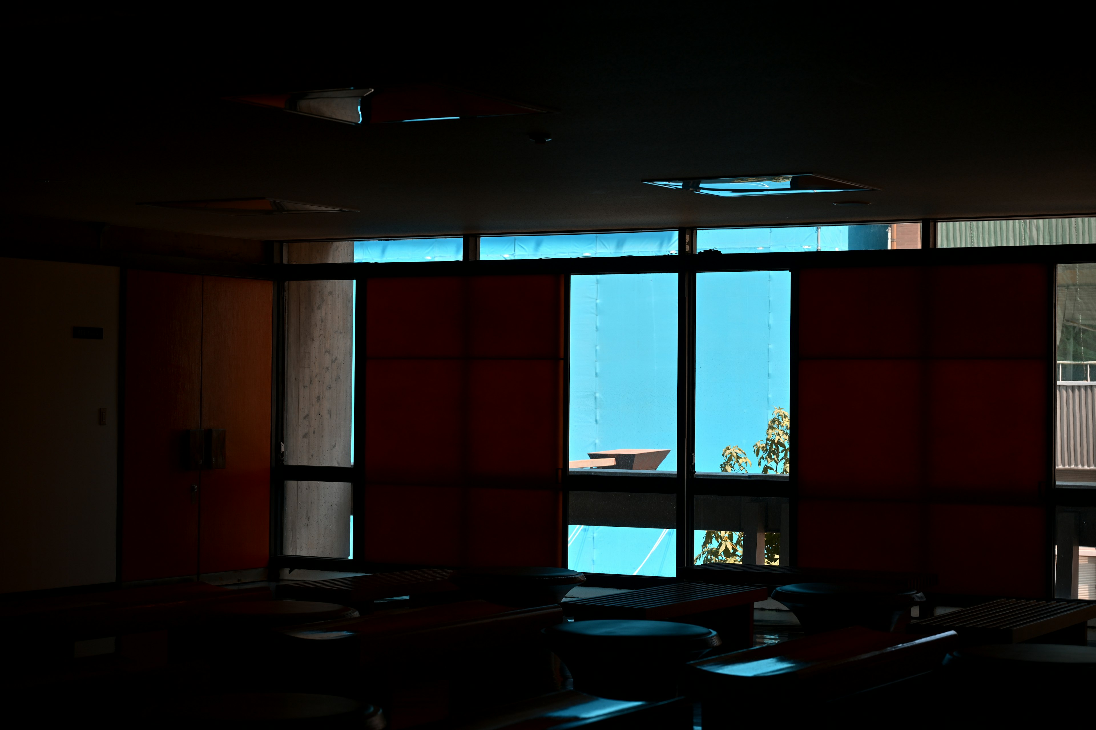 Interior débilmente iluminado con vista a una pared azul y cortinas rojas