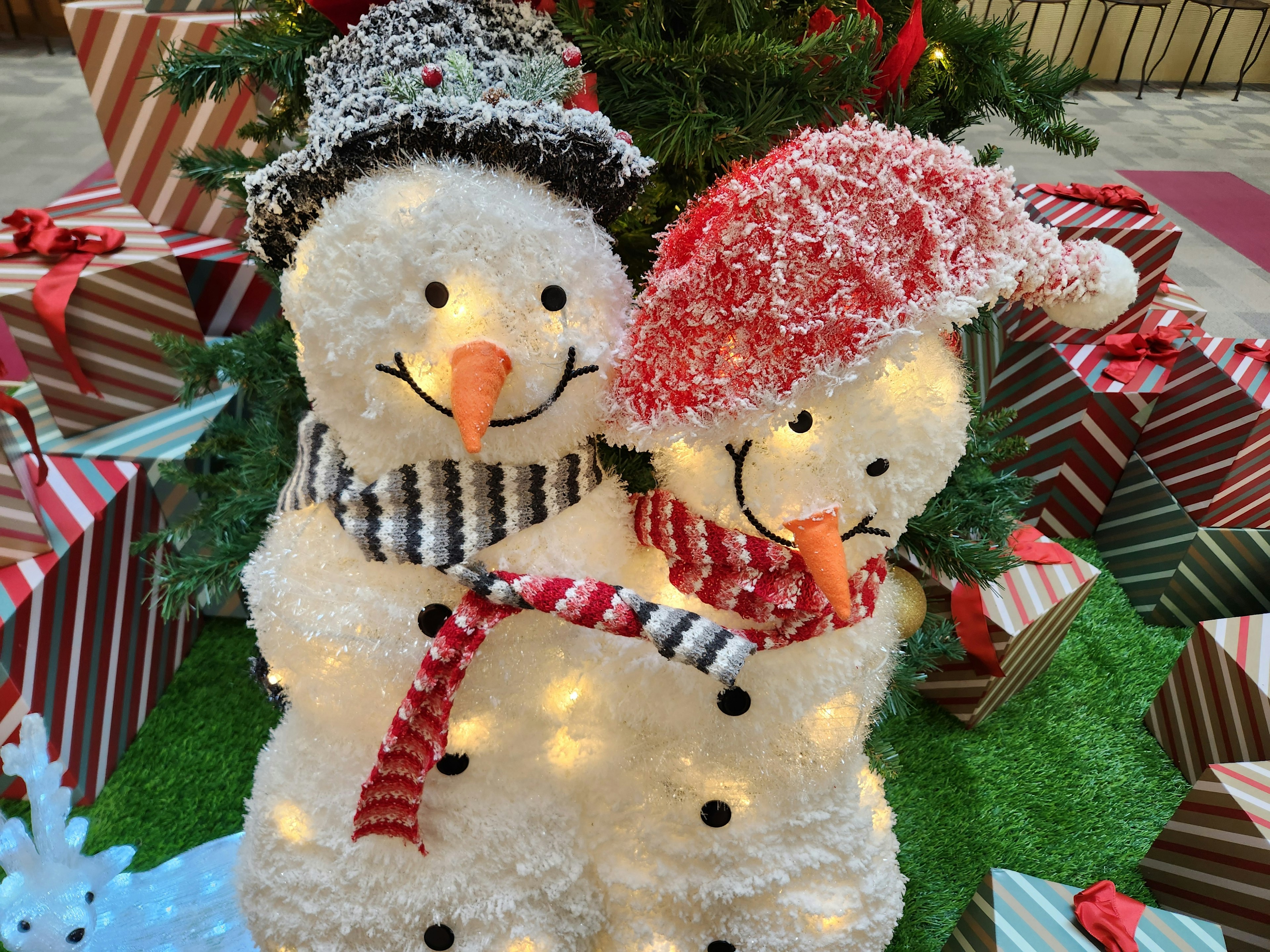 Couple of snowmen with festive hats and scarves surrounded by Christmas gifts