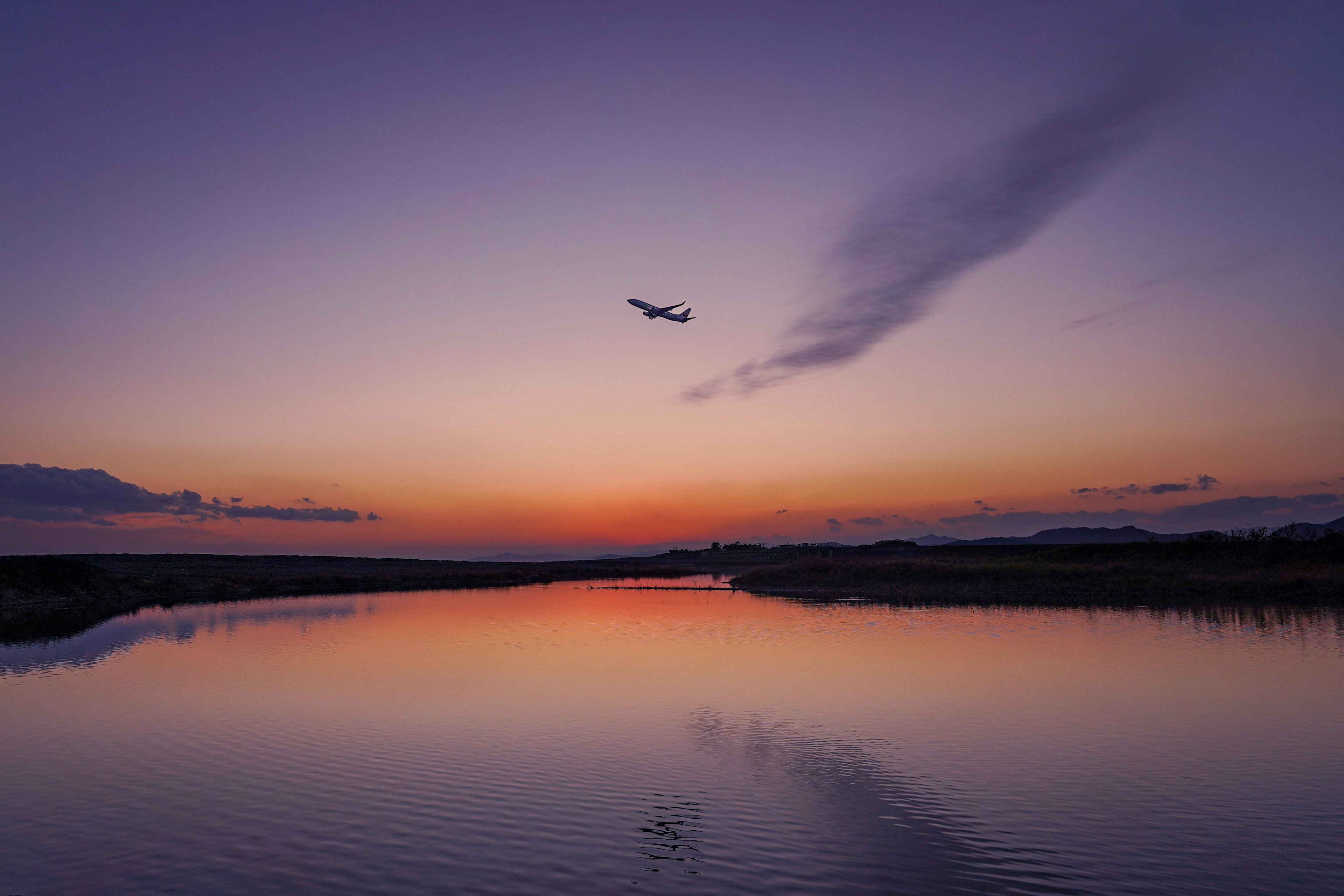 夕焼けの空に飛行機が飛ぶ静かな湖の風景