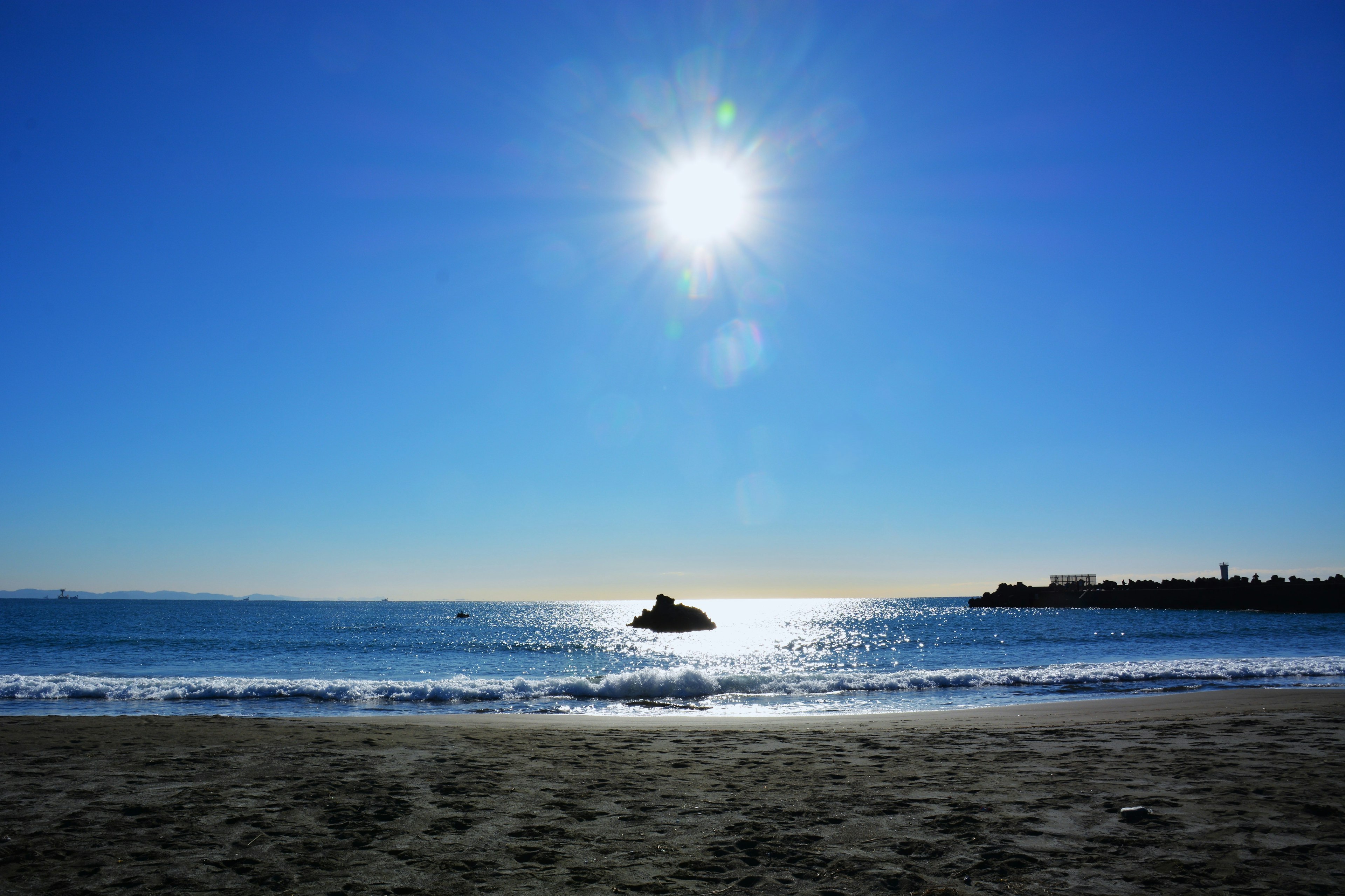 Cielo azul brillante con sol resplandeciente sobre olas tranquilas y playa de arena