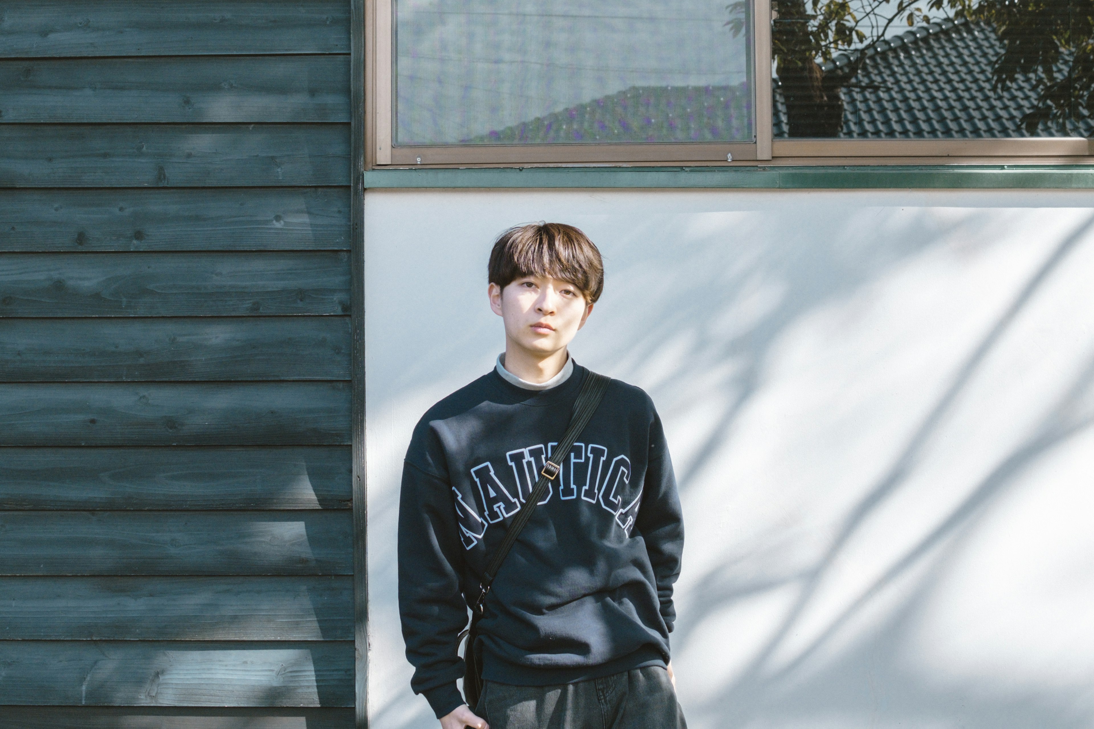 Young man standing in front of a blue wall wearing casual attire sunlight casting shadows