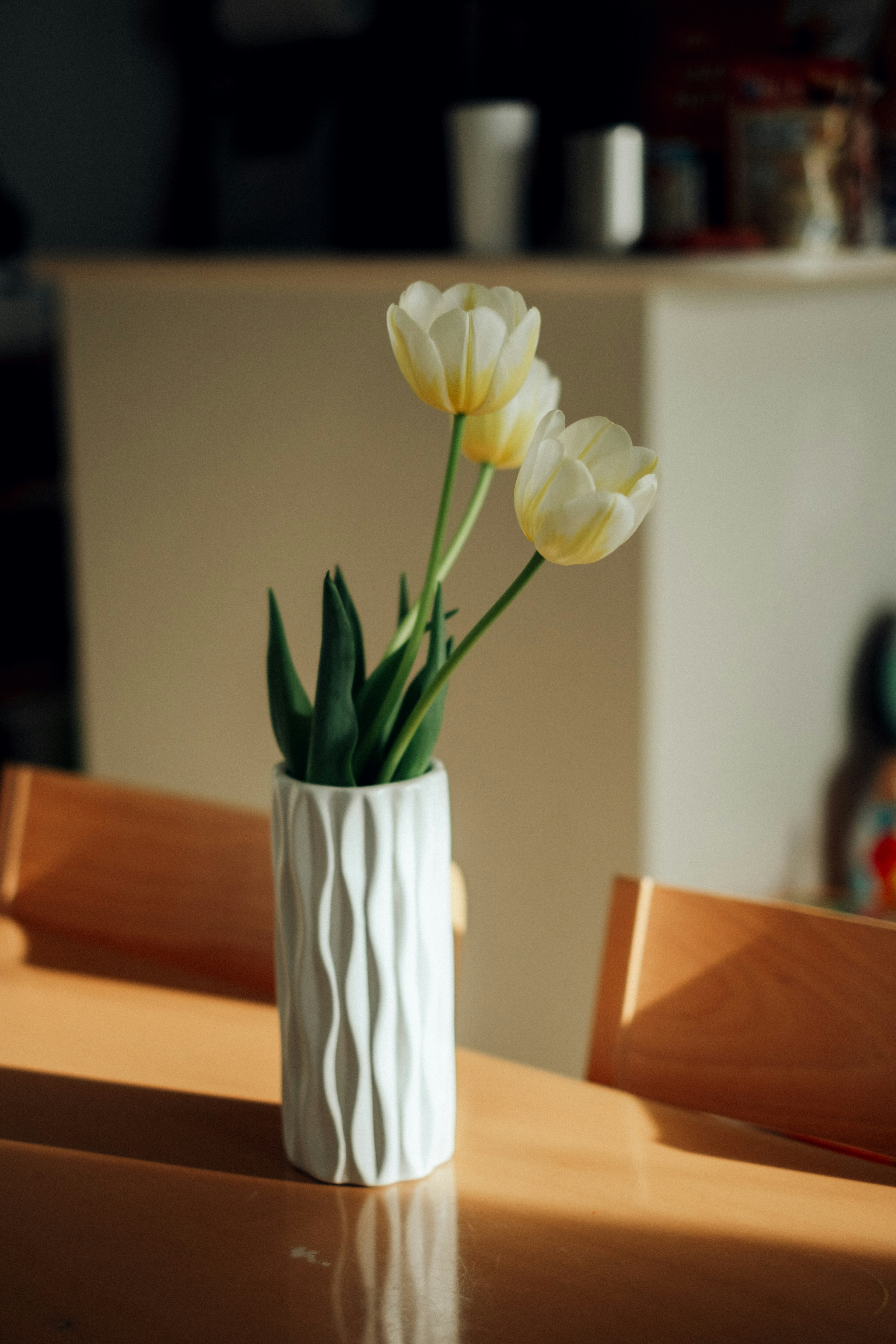 Un décor de table simple et élégant avec un vase blanc contenant des tulipes jaunes