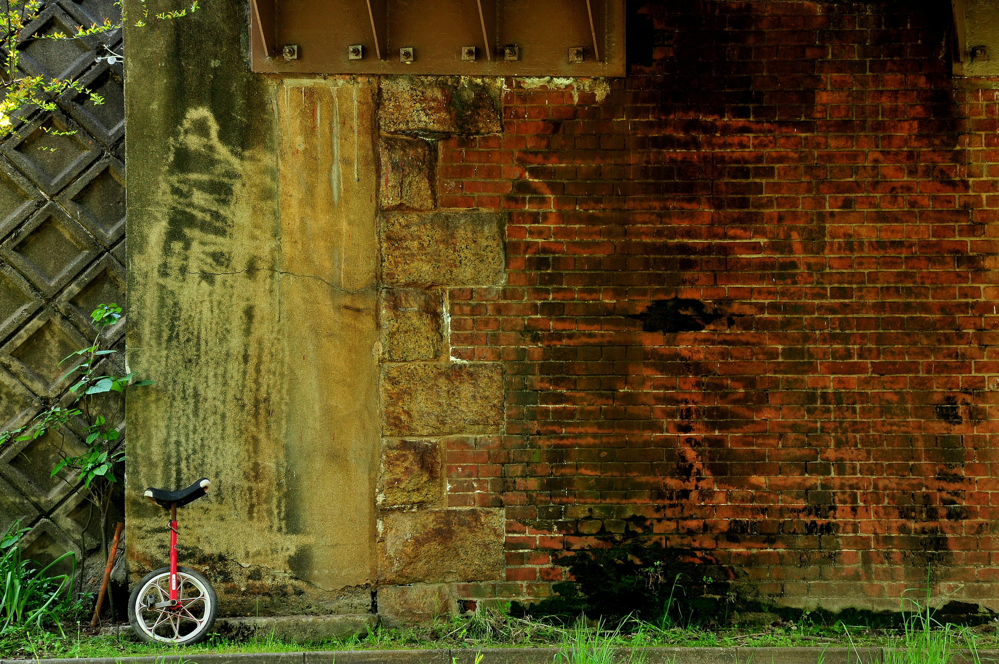 Un monocycle placé à côté d'un mur en briques vieillies avec des touffes d'herbe verte