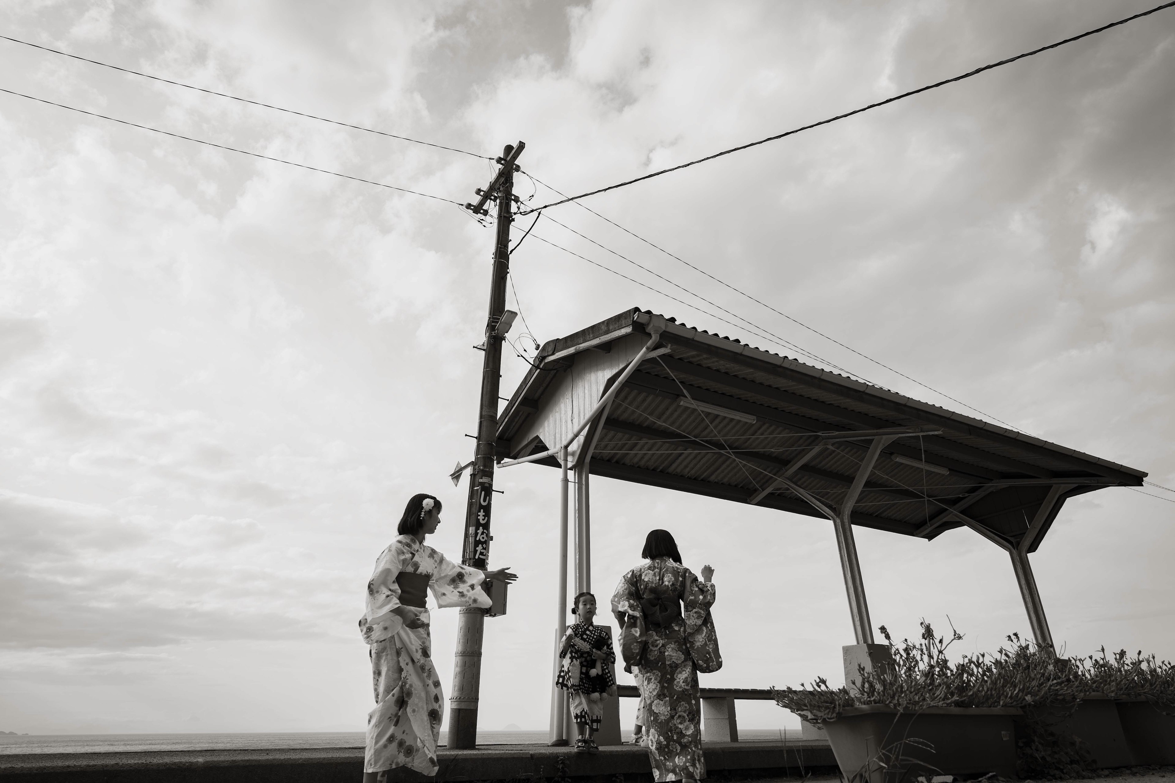 Scena in bianco e nero con donne in kimono tradizionali presso una fermata del treno