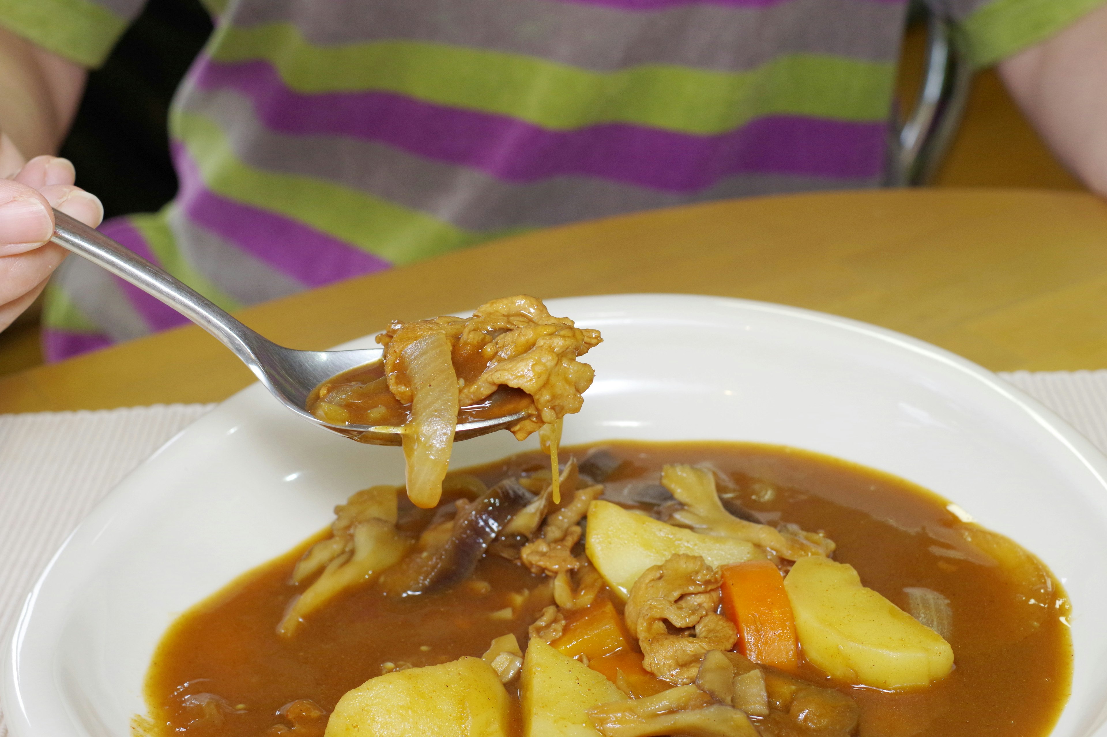 Child's hand holding a spoon with a bowl of vegetable and meat stew