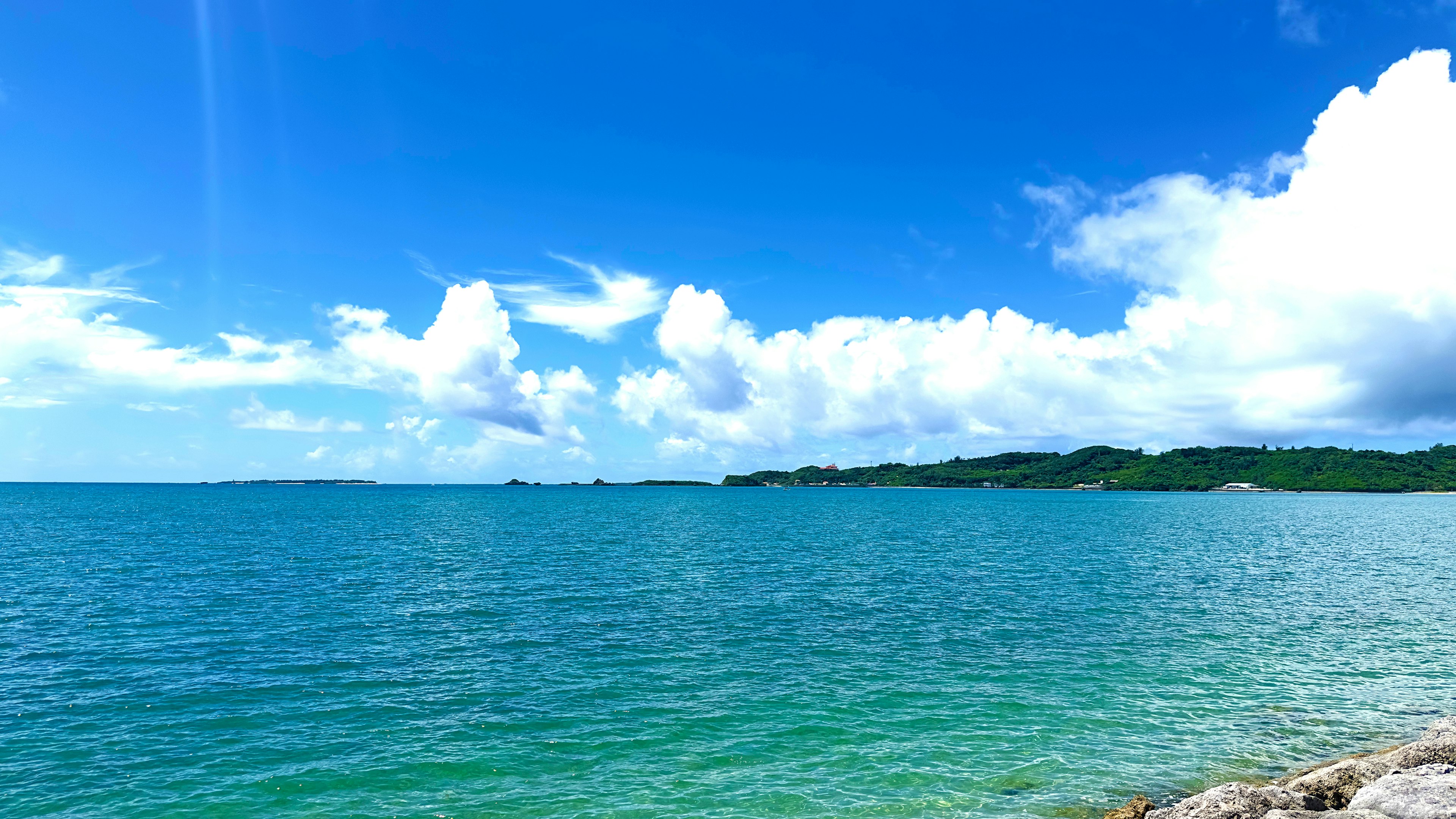 Vibrant blue sea under a clear sky with scattered clouds