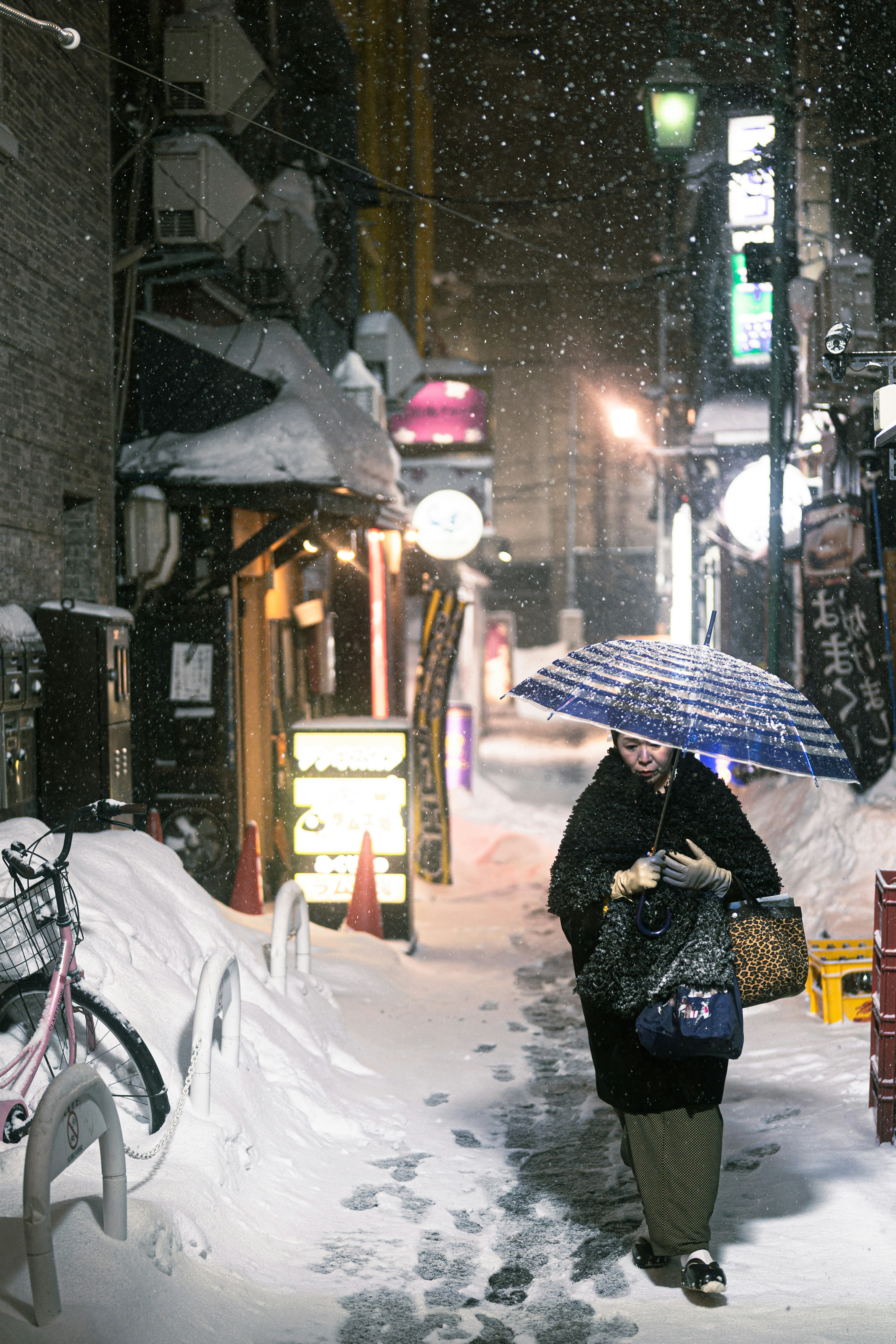 A woman walking in the snow holding an umbrella on a narrow street