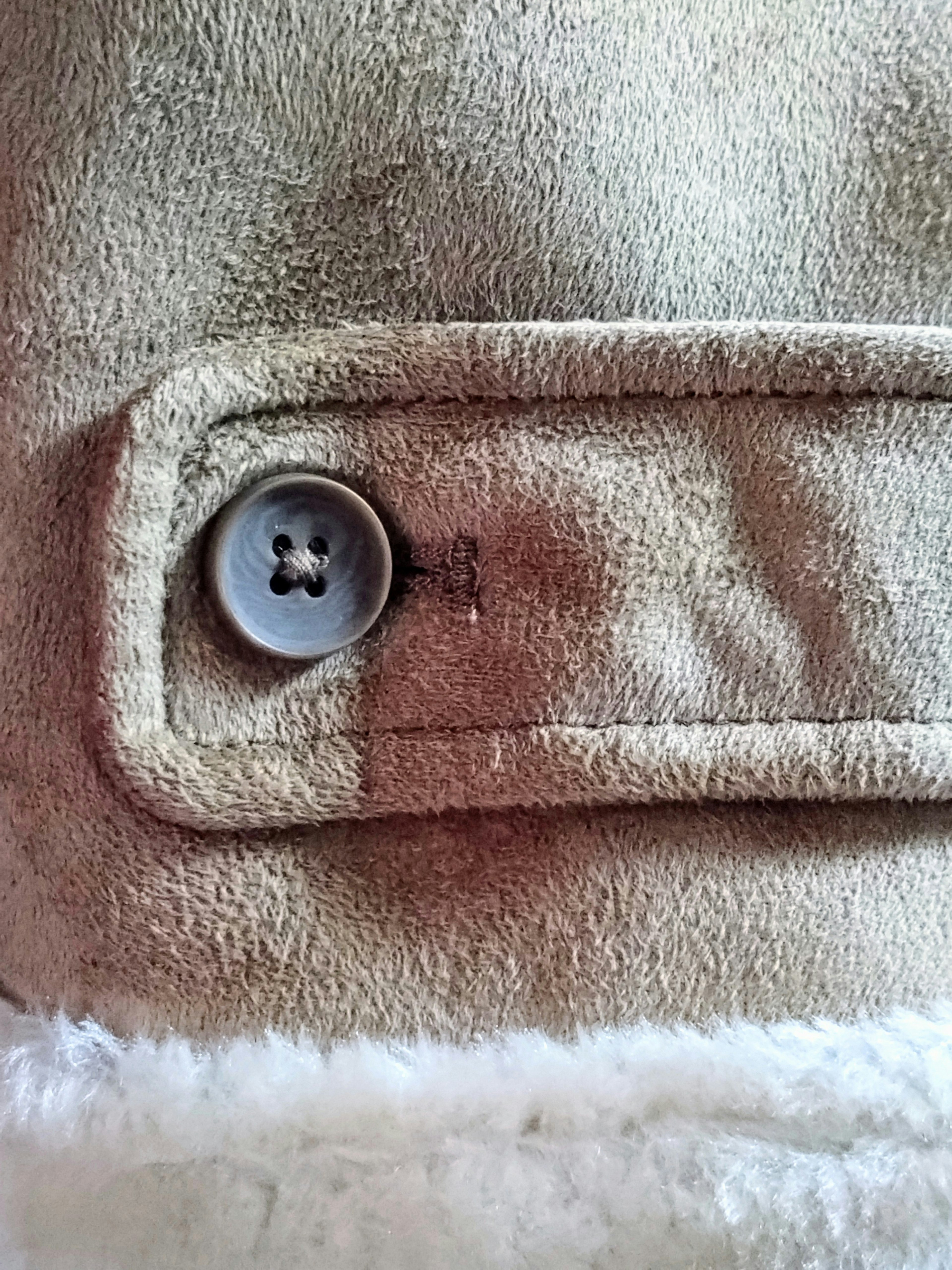 Close-up tombol jaket beige menunjukkan detail kain lembut dan tombol