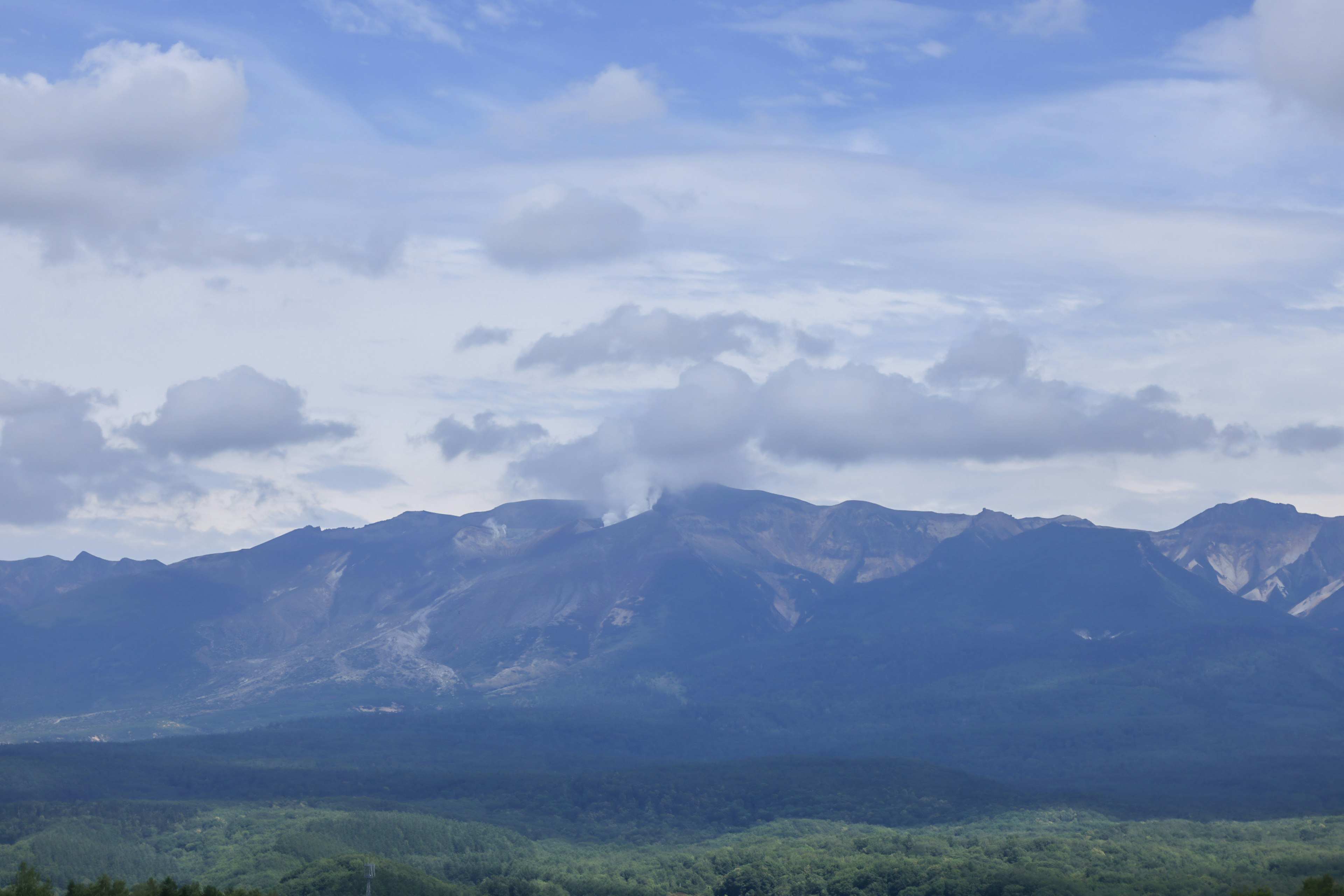 青い空と雲に囲まれた緑の山々の風景